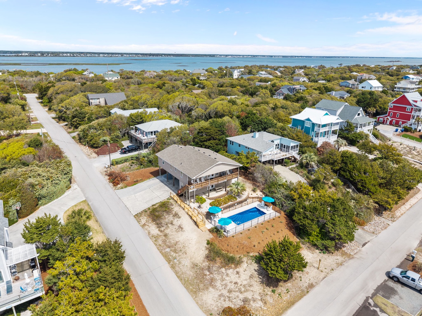 Aerial view of coastal vacation home with private pool nestled among mature trees, just steps from pristine waters.