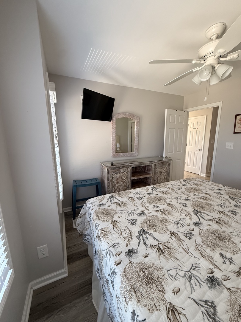 Your serene bedroom features a plush bed with charming nature-inspired linens, soft lighting from a ceiling fan, a wall-mounted TV for cozy nights in, and plenty of closet space for easy unpacking.