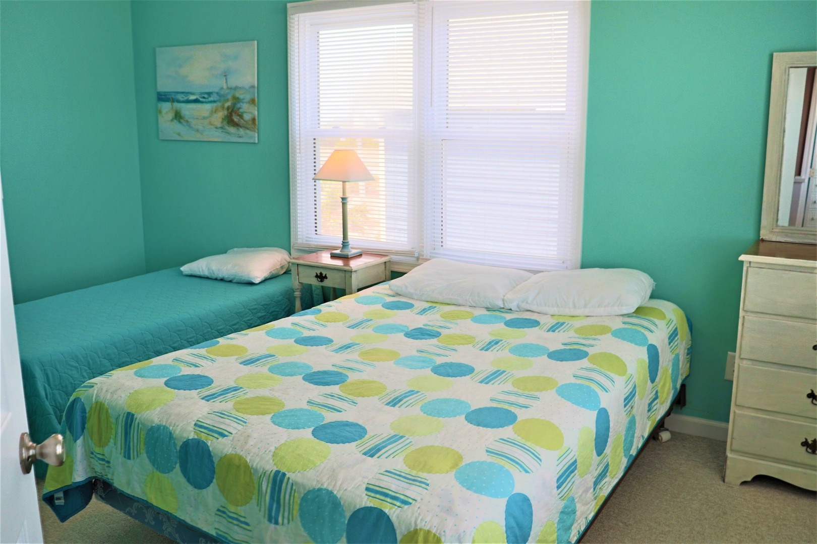 Relax in this cheerful twin bedroom where turquoise walls and ocean artwork create a coastal vibe perfect for peaceful nights.