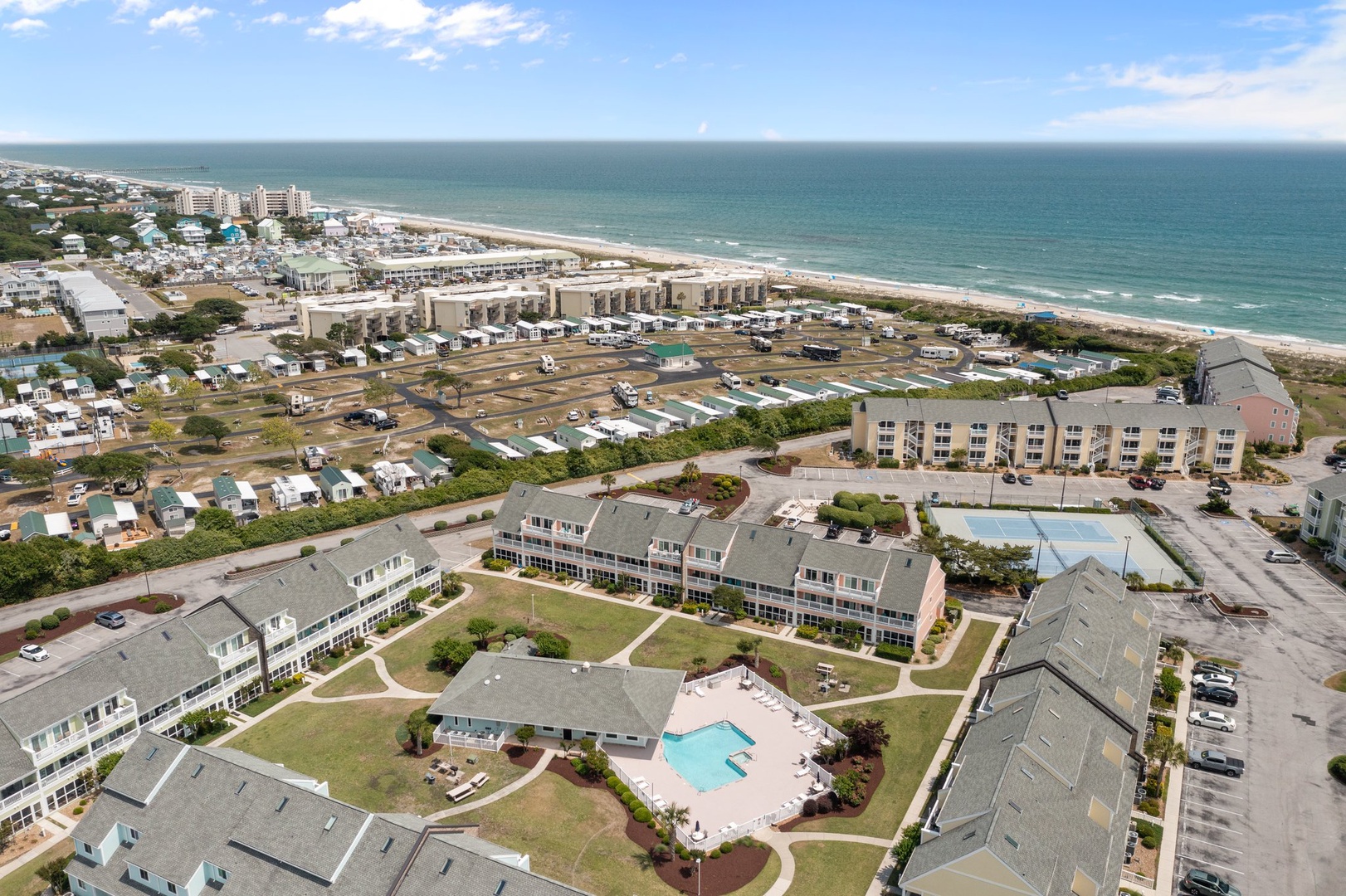 Aerial view of beachfront resort complex with swimming pool, surrounded by coastal community and pristine sandy beach.