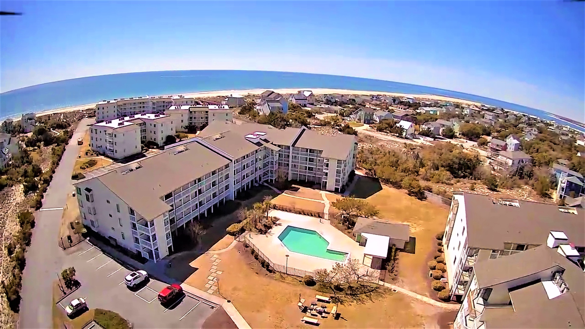 Aerial view of beachfront resort complex with swimming pool, just steps from pristine sandy shores and sparkling ocean waters.
