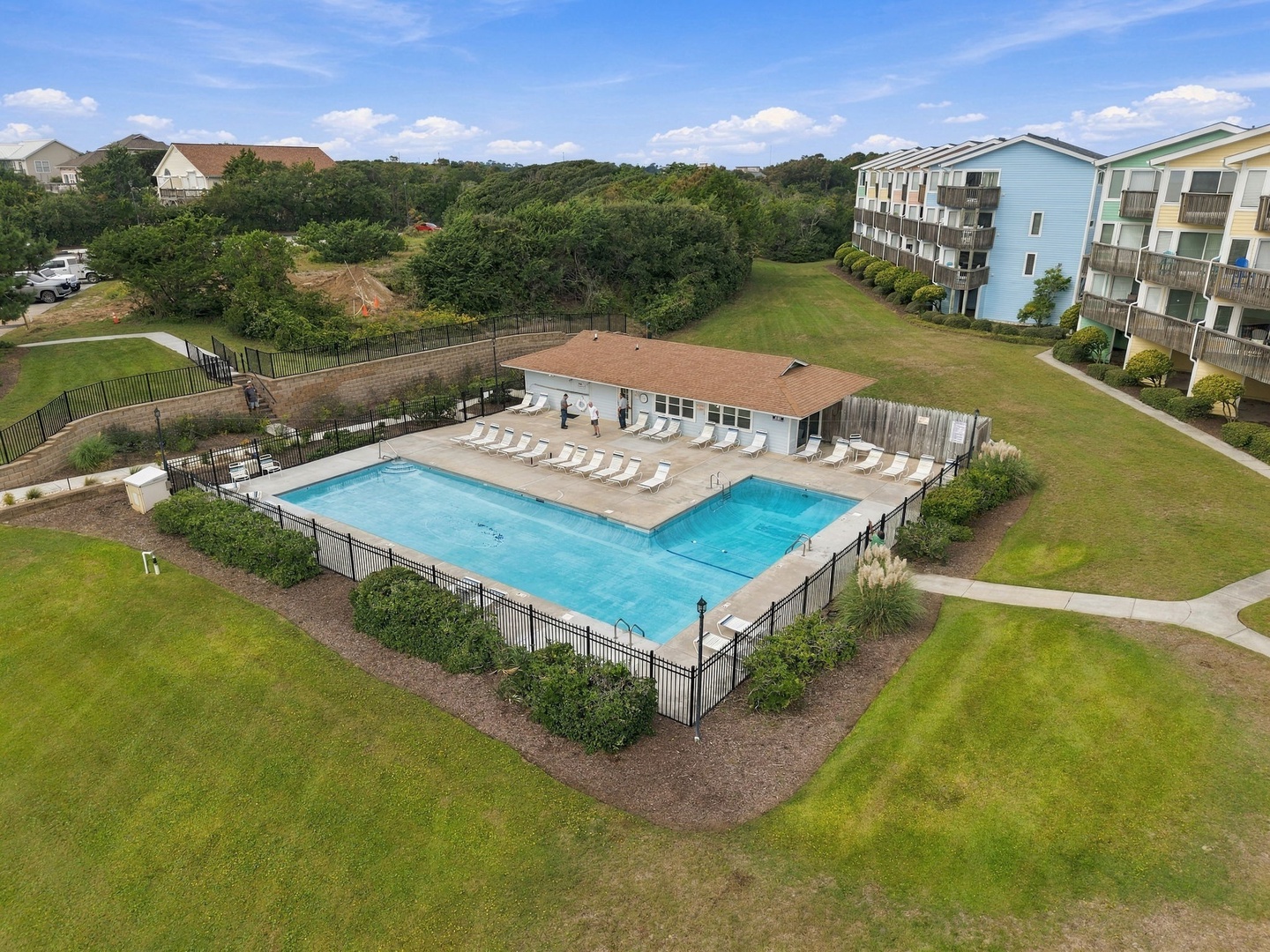An aerial view of the property reveals a welcoming pool complex surrounded by green space, with multi-story vacation buildings nearby and natural wooded areas stretching beyond the grounds.