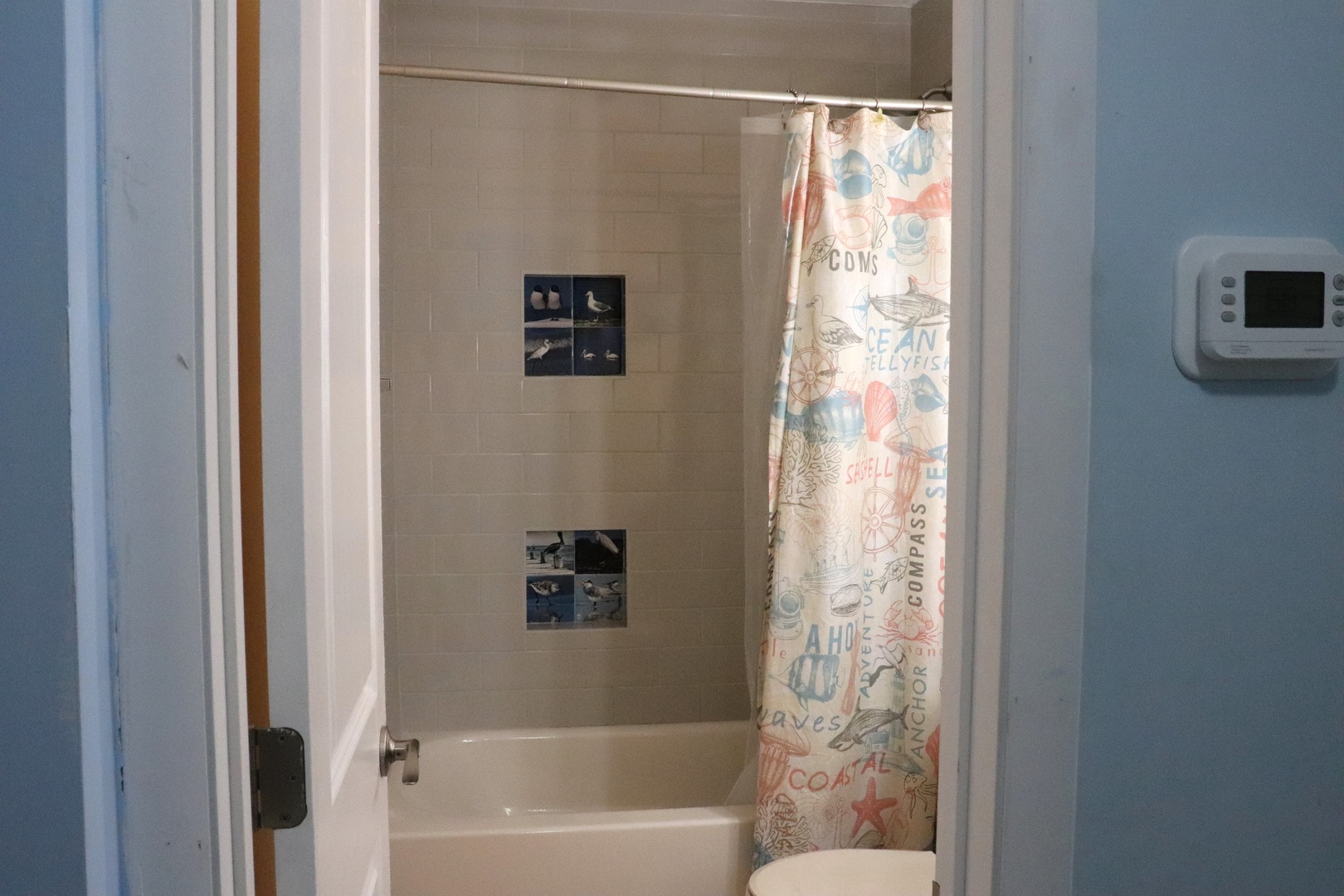 Your private bathroom features a tub-shower combo with coastal-themed curtain, clean tile surround, and modern fixtures for a refreshing start to your beach days.