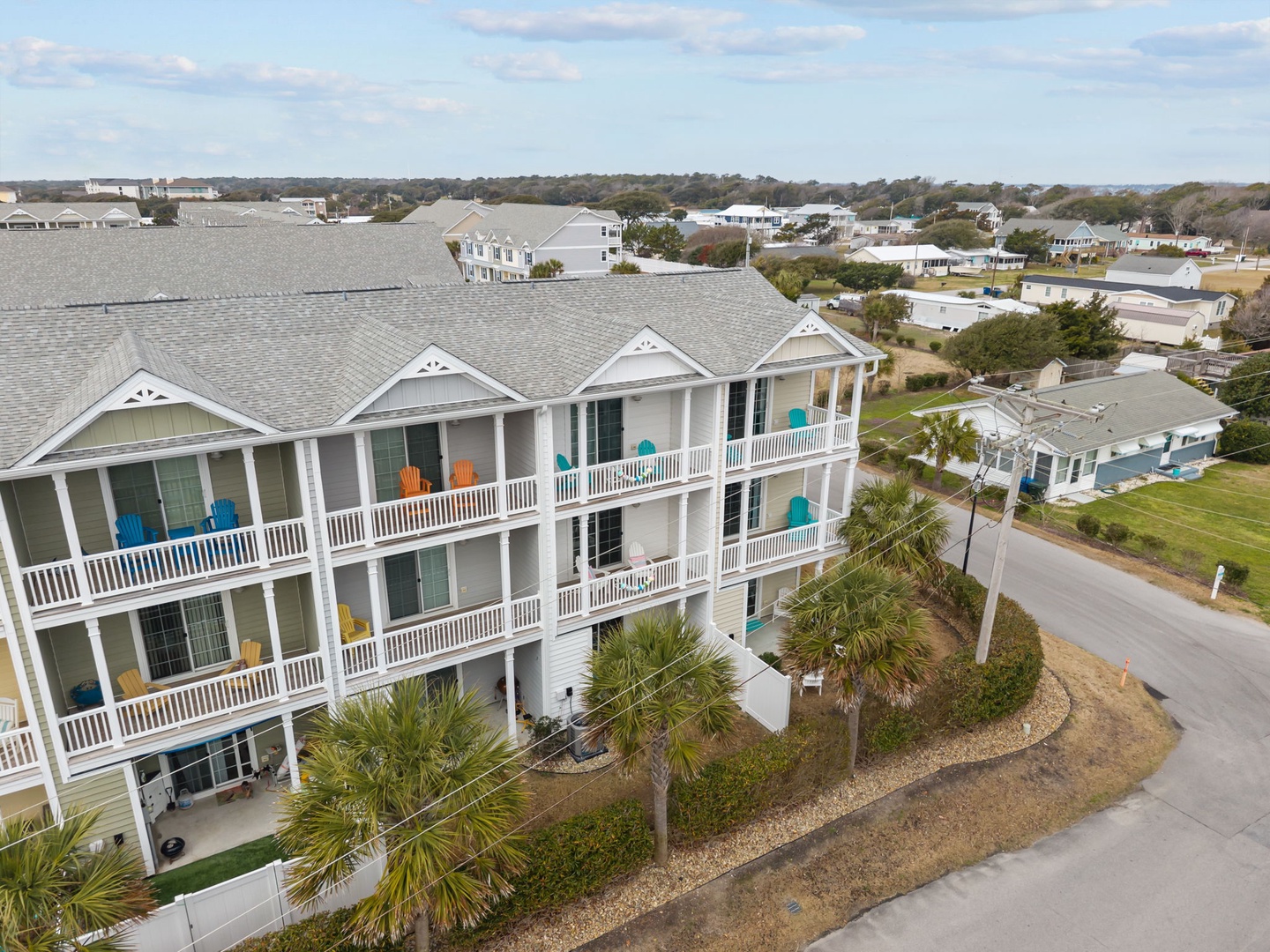 Charming coastal resort building featuring multiple balconies with colorful chairs, surrounded by palm trees and residential neighborhood views.