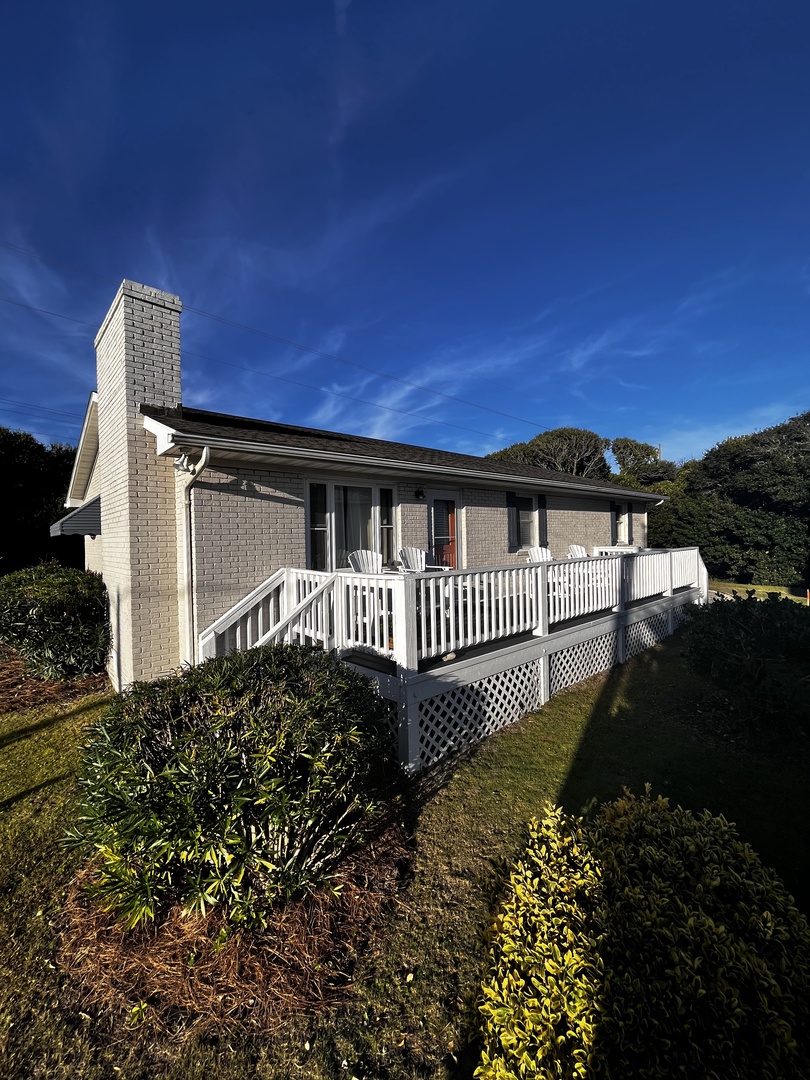 A charming white property surrounded by mature trees and landscaped gardens under a brilliant blue sky.