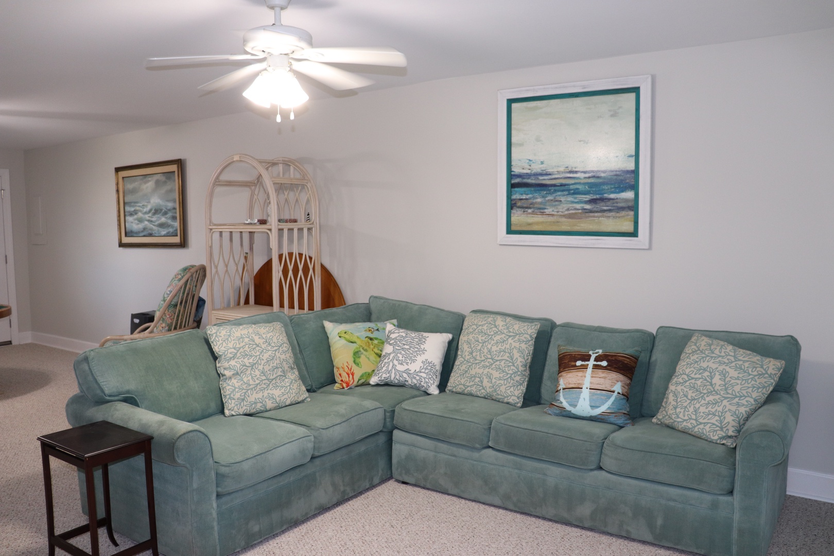 Relax in your comfortable living room featuring a plush sectional sofa, coastal artwork, and gentle ceiling fan for your perfect getaway.