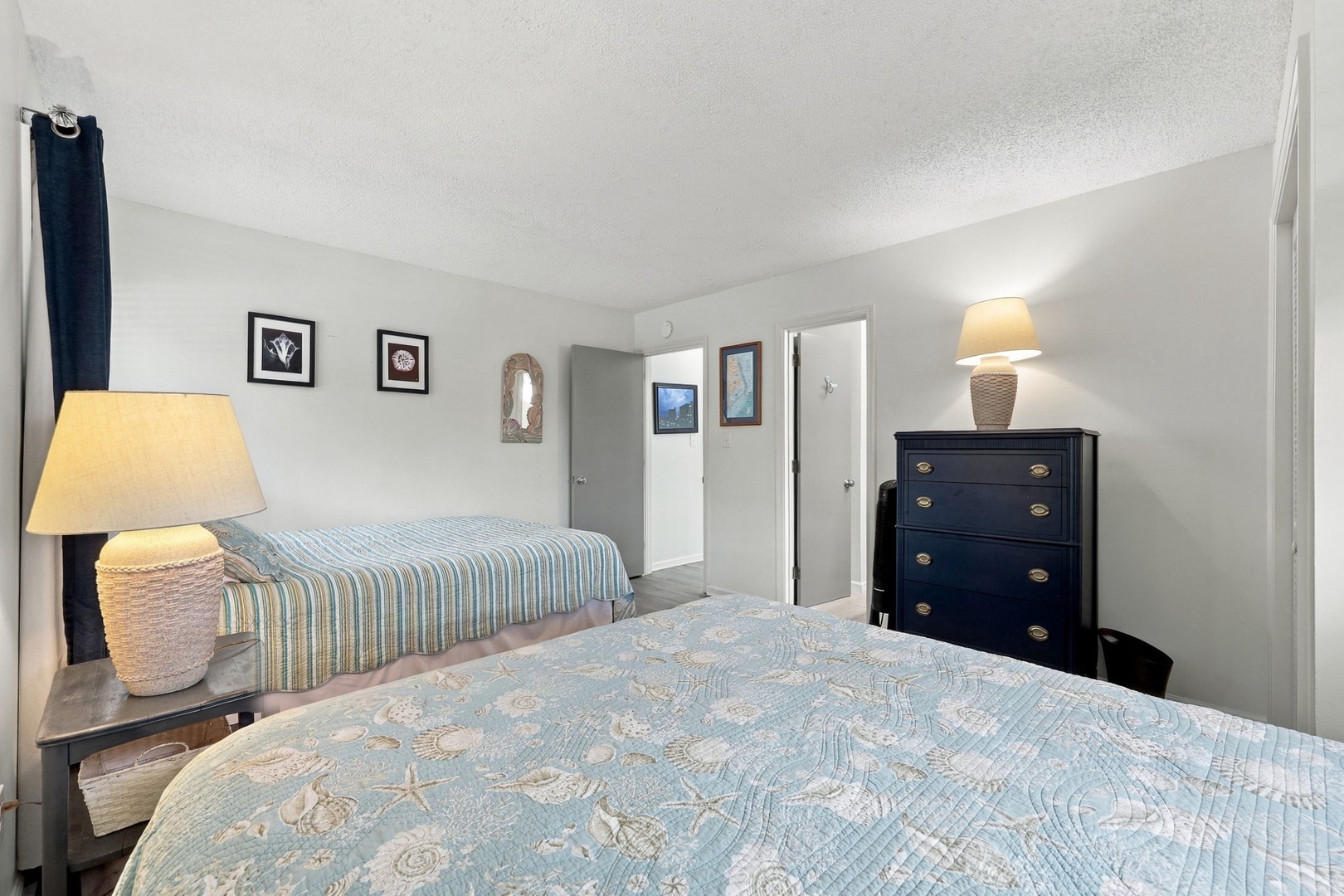 Unwind in your coastal-themed bedroom with two comfortable beds and soft bedside lighting that creates a peaceful ambiance for your stay.