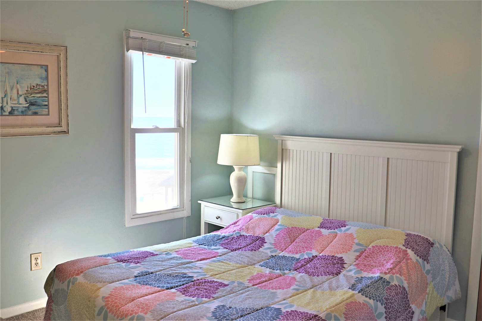 Drift off to sleep in this peaceful bedroom with soothing seafoam walls, natural light, and charming coastal artwork creating your perfect retreat.