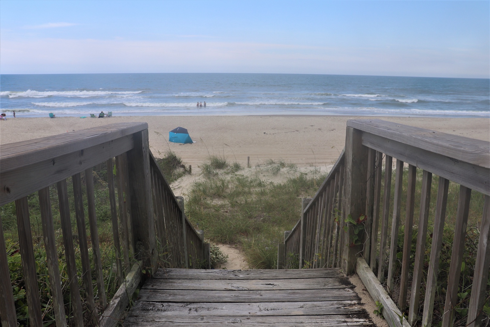 Wooden boardwalk leads directly to pristine sandy beach with gentle waves and endless ocean views.