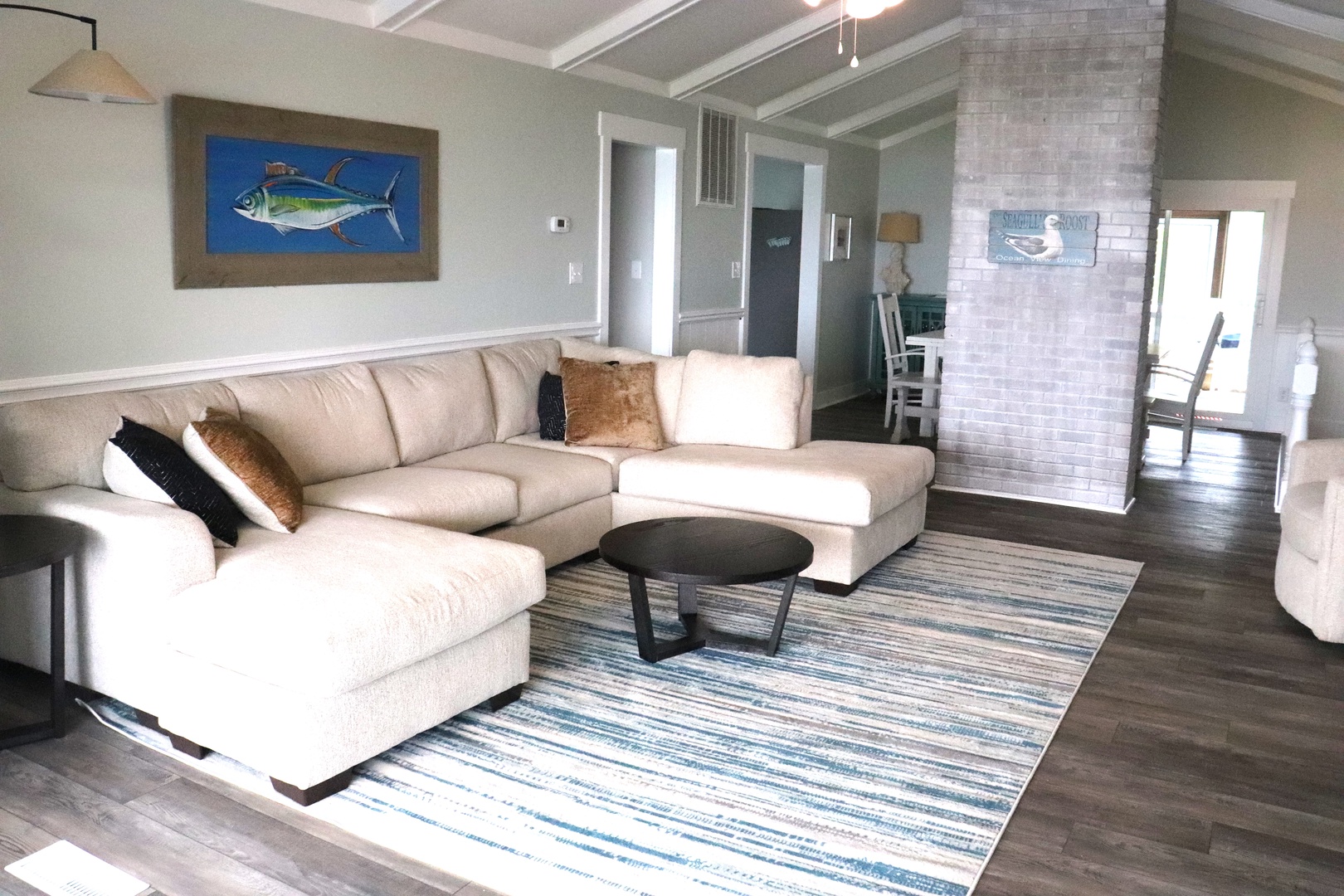 Sink into the plush sectional sofa and unwind in this coastal-inspired living space with ocean-themed art and brick fireplace.