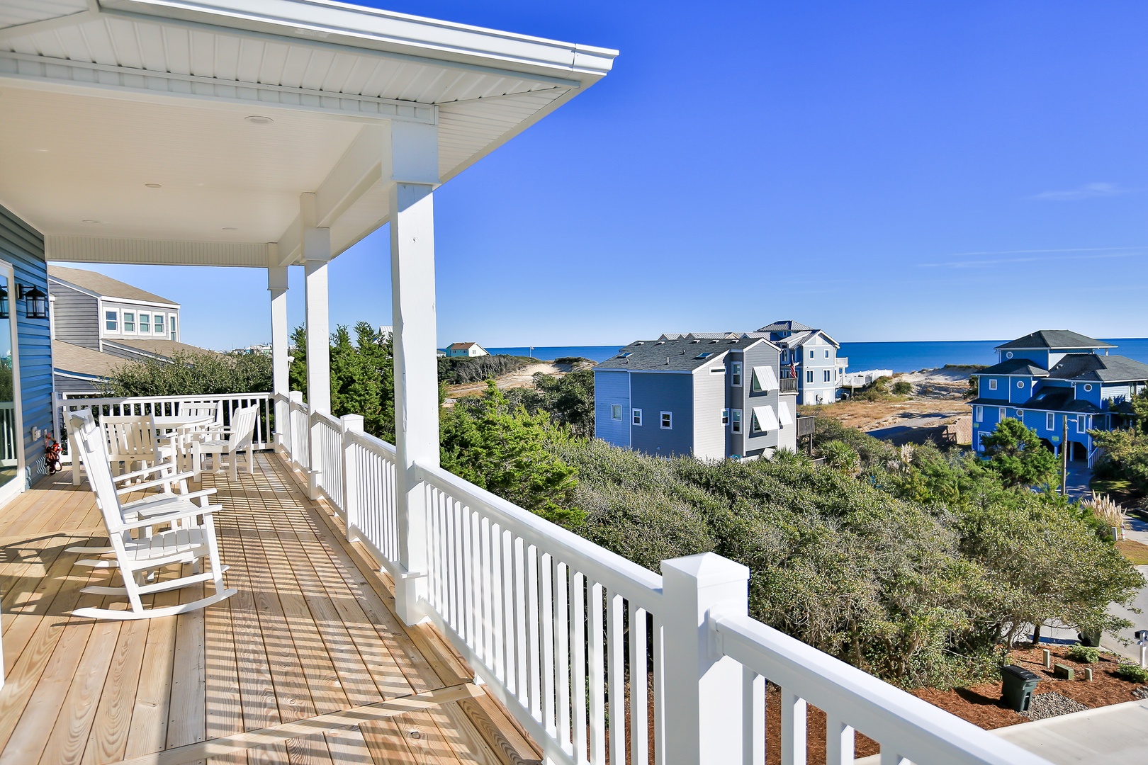 Your private deck with rocking chairs overlooks colorful beach homes and distant ocean views—perfect for morning coffee or evening relaxation.