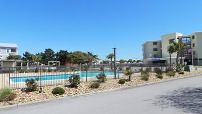 Modern apartment complex with refreshing swimming pool surrounded by Mediterranean landscaping and contemporary buildings in a peaceful residential setting.