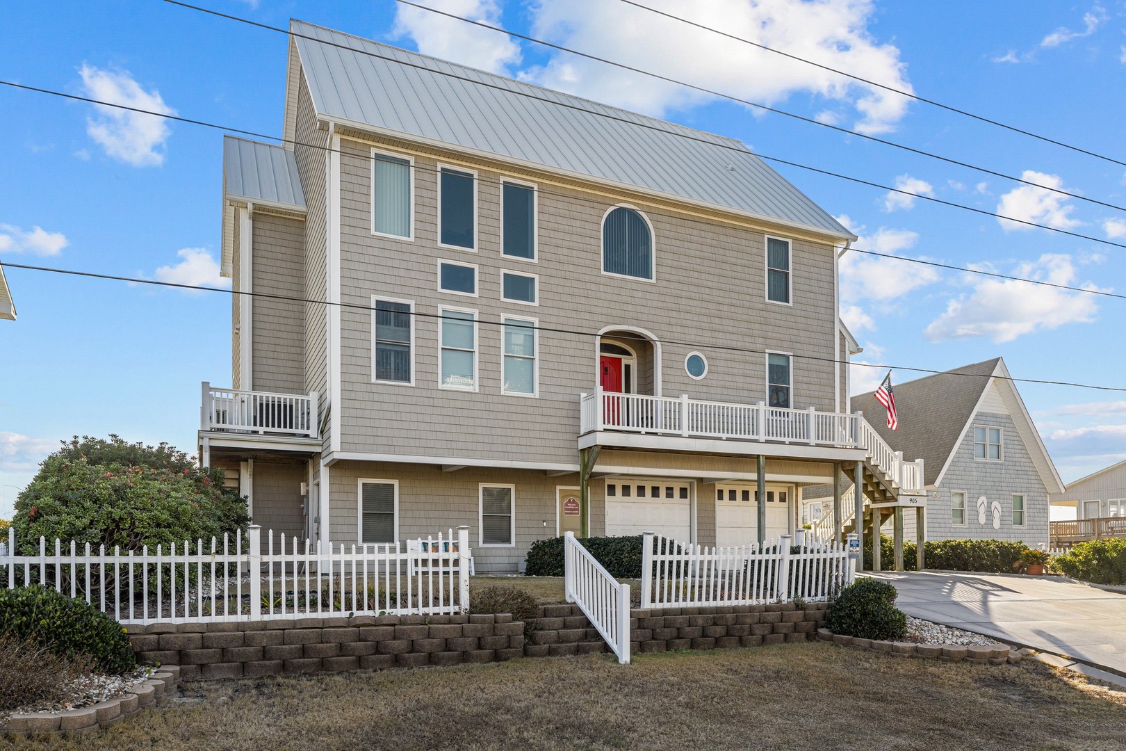 A stunning three-story coastal home with classic shingle siding and spacious wraparound balcony, perfectly positioned in a charming neighborhood setting.