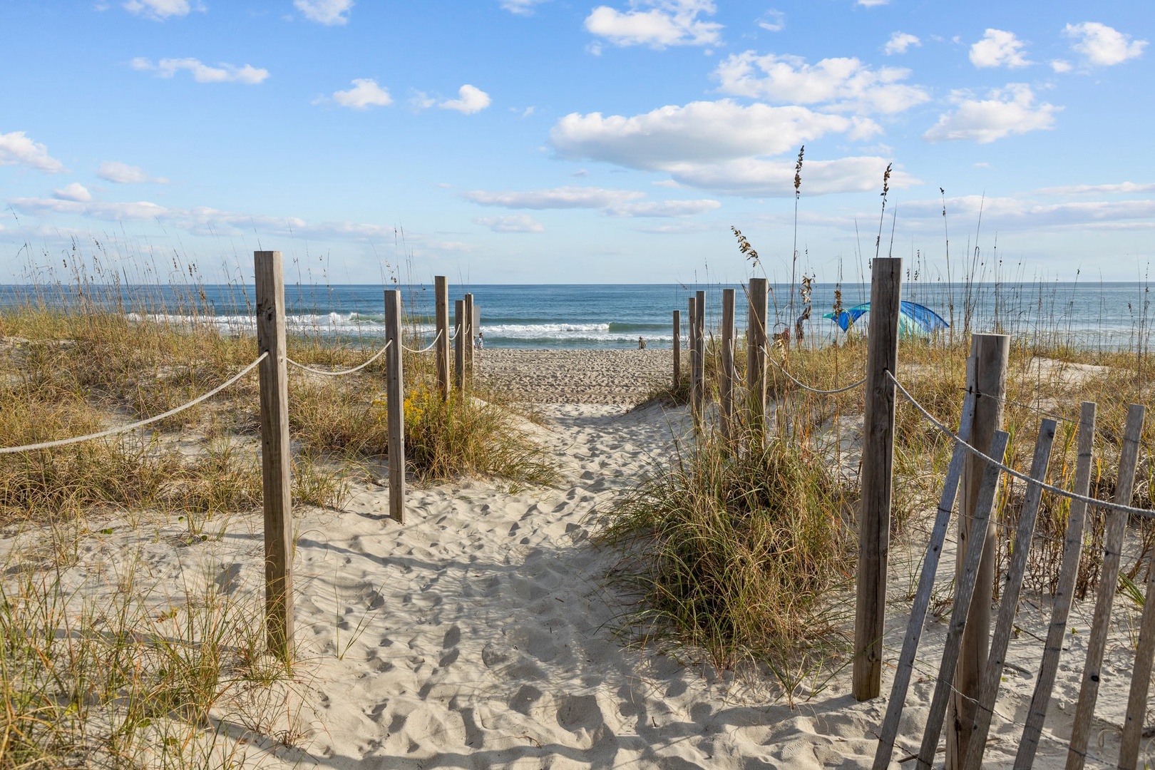 A scenic boardwalk path leads through coastal dunes to pristine white sand beaches and turquoise waters.