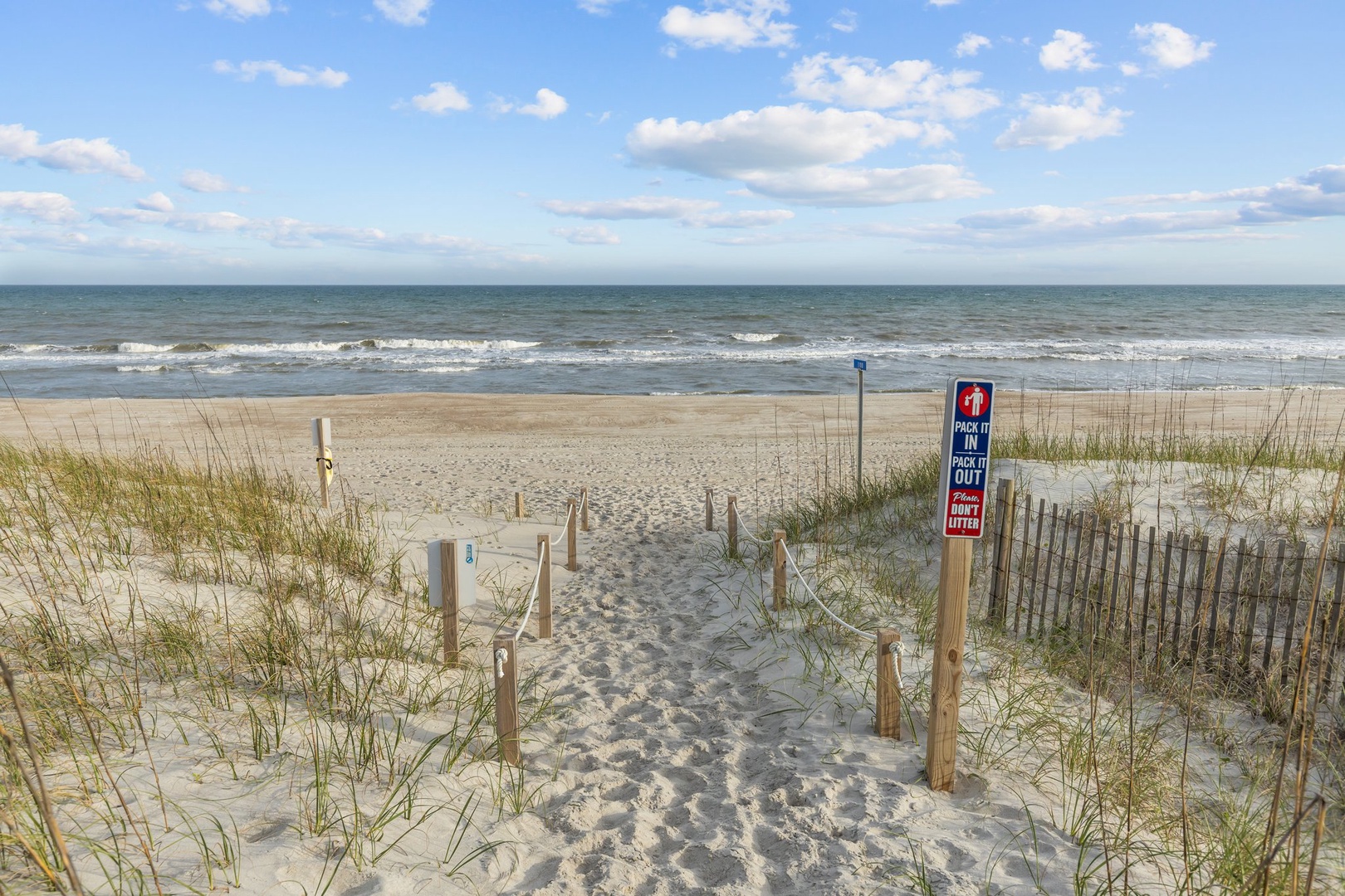 Pristine sandy beach with dune walkway leading to gentle waves under a beautiful cloudy sky.