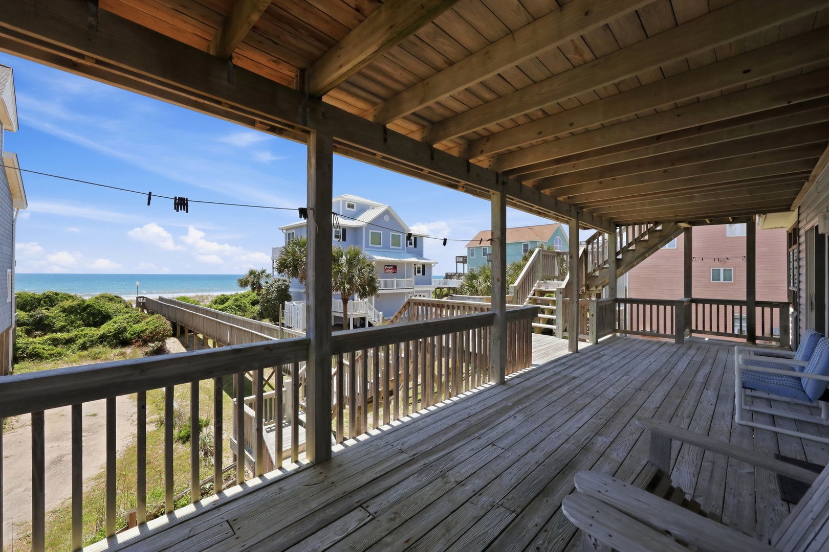 Covered deck with beachfront access and ocean views in a coastal neighborhood setting, featuring natural wood construction and convenient boardwalk pathway to the shore.