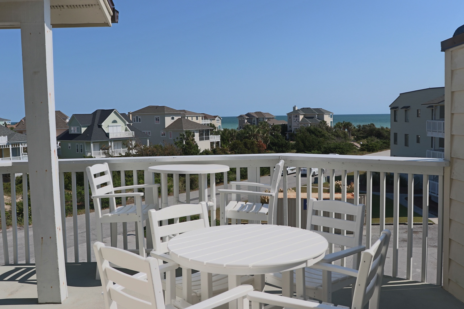 Your private balcony dining space offers glimpses of ocean blue through coastal homes and swaying palms.