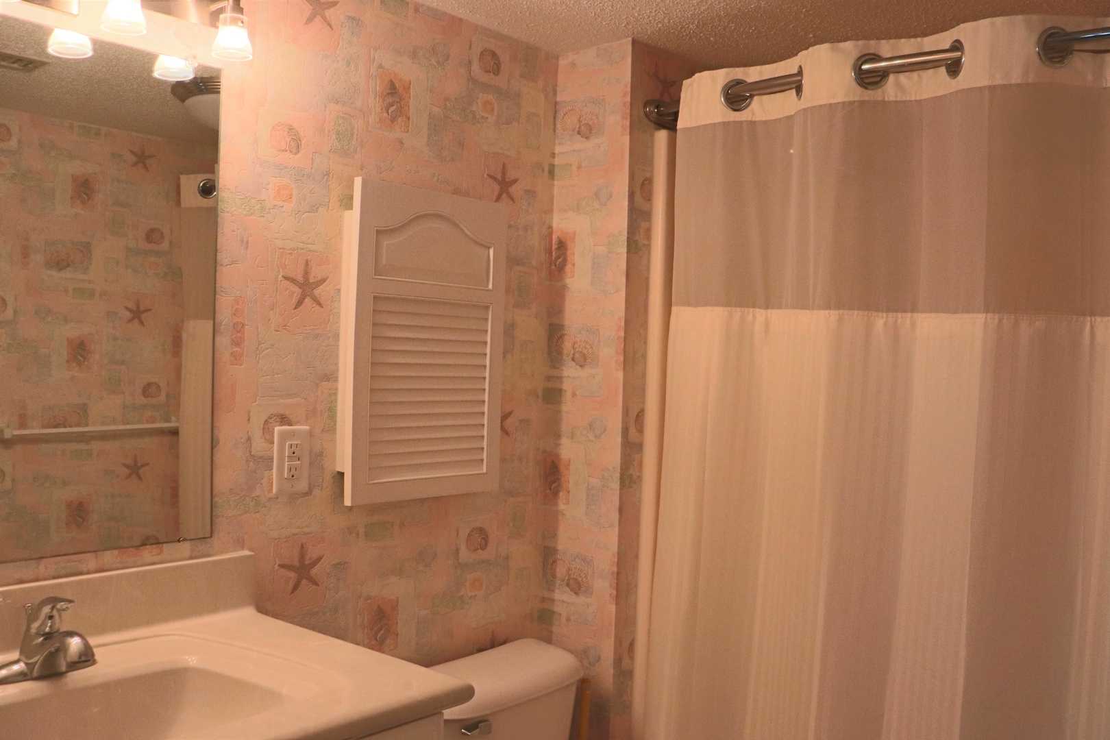 Refresh in your private bathroom featuring coastal-themed wallpaper and a convenient shower-tub combo for relaxing after beach adventures.