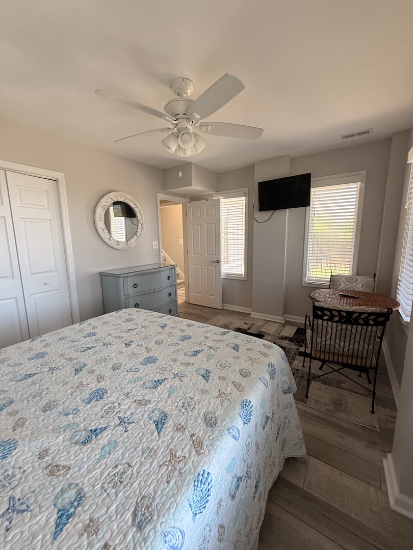 Your cozy bedroom features a comfortable bed with charming coastal bedding, natural light from double windows, and convenient in-room laundry facilities for a relaxing, home-like stay.