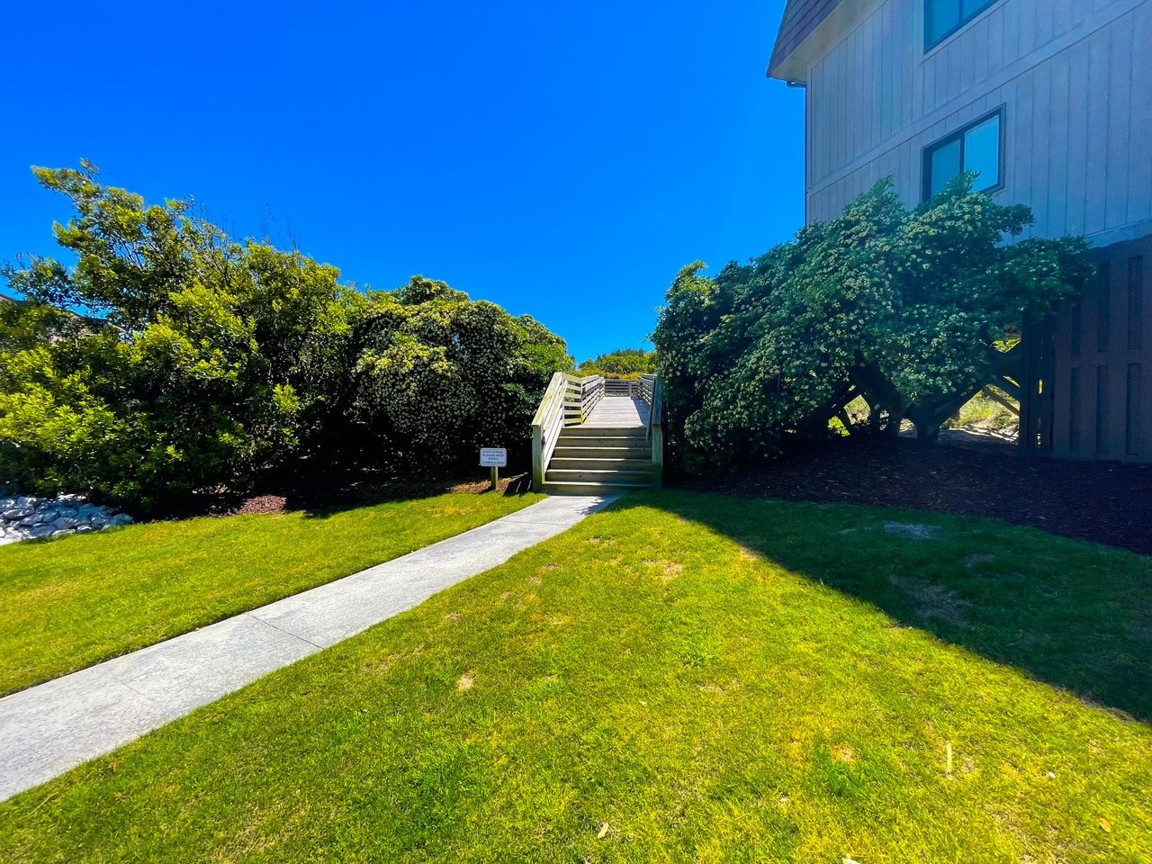 Modern coastal property featuring bright blue skies, lush green landscaping, and a welcoming pathway leading to your vacation retreat.