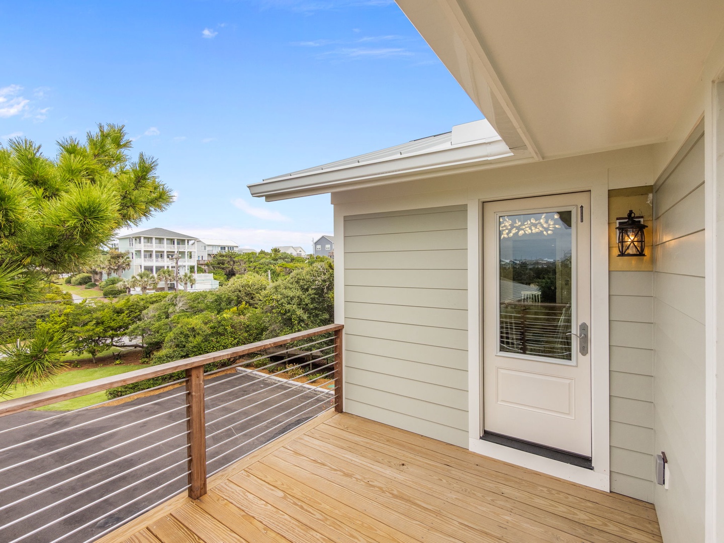 Coastal property entrance with modern deck and tropical landscaping under clear blue skies.