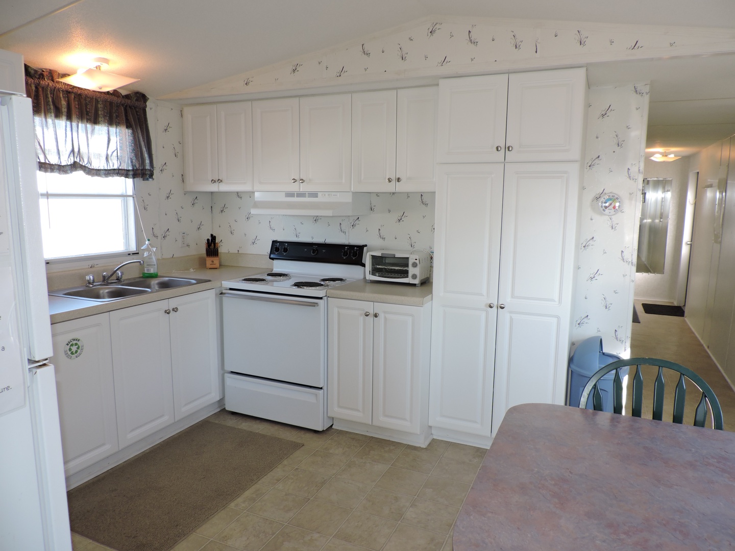 Step into your fully equipped kitchen with crisp white cabinets, modern appliances, and charming bird-patterned wallpaper creating a bright, welcoming space for your culinary adventures.