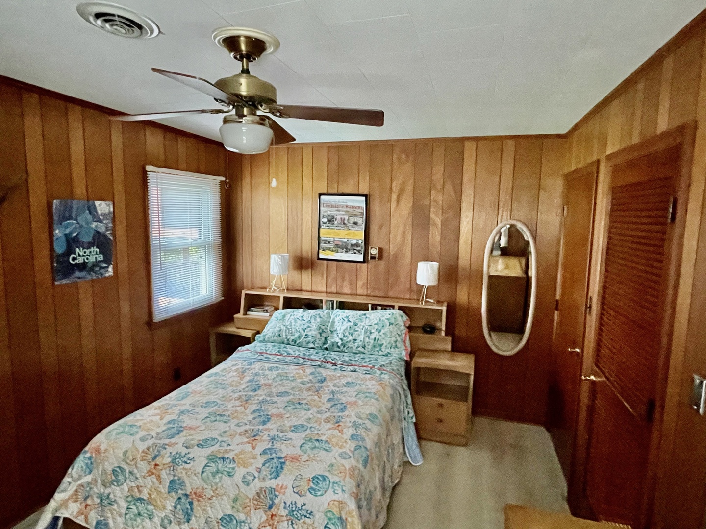 Relax in your cozy wood-paneled bedroom with tropical bedding, ceiling fan, and vintage charm that creates the perfect retreat.