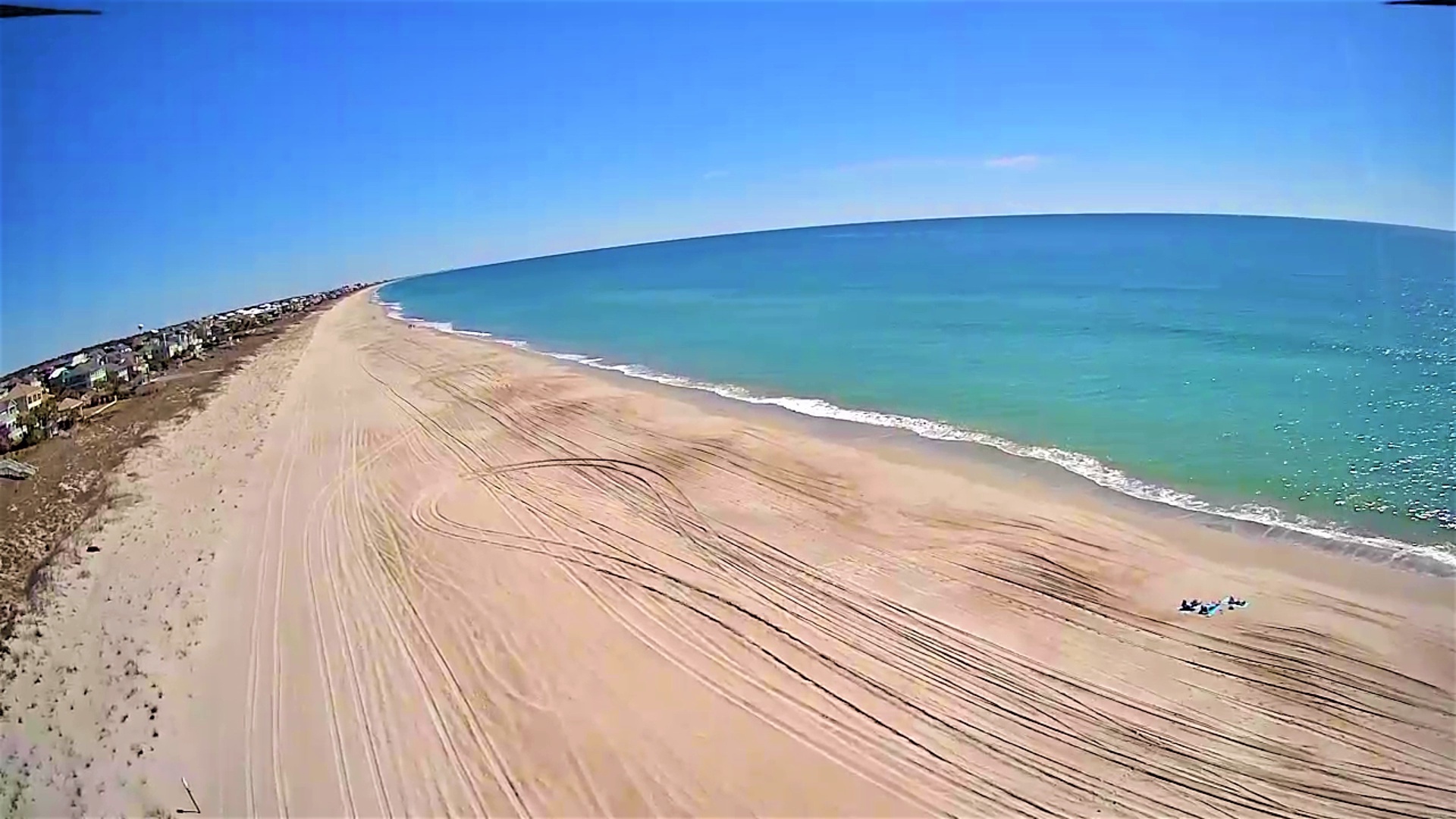 Sweeping aerial view reveals miles of pristine sandy coastline meeting crystal-clear turquoise waters along this stunning beachfront destination.
