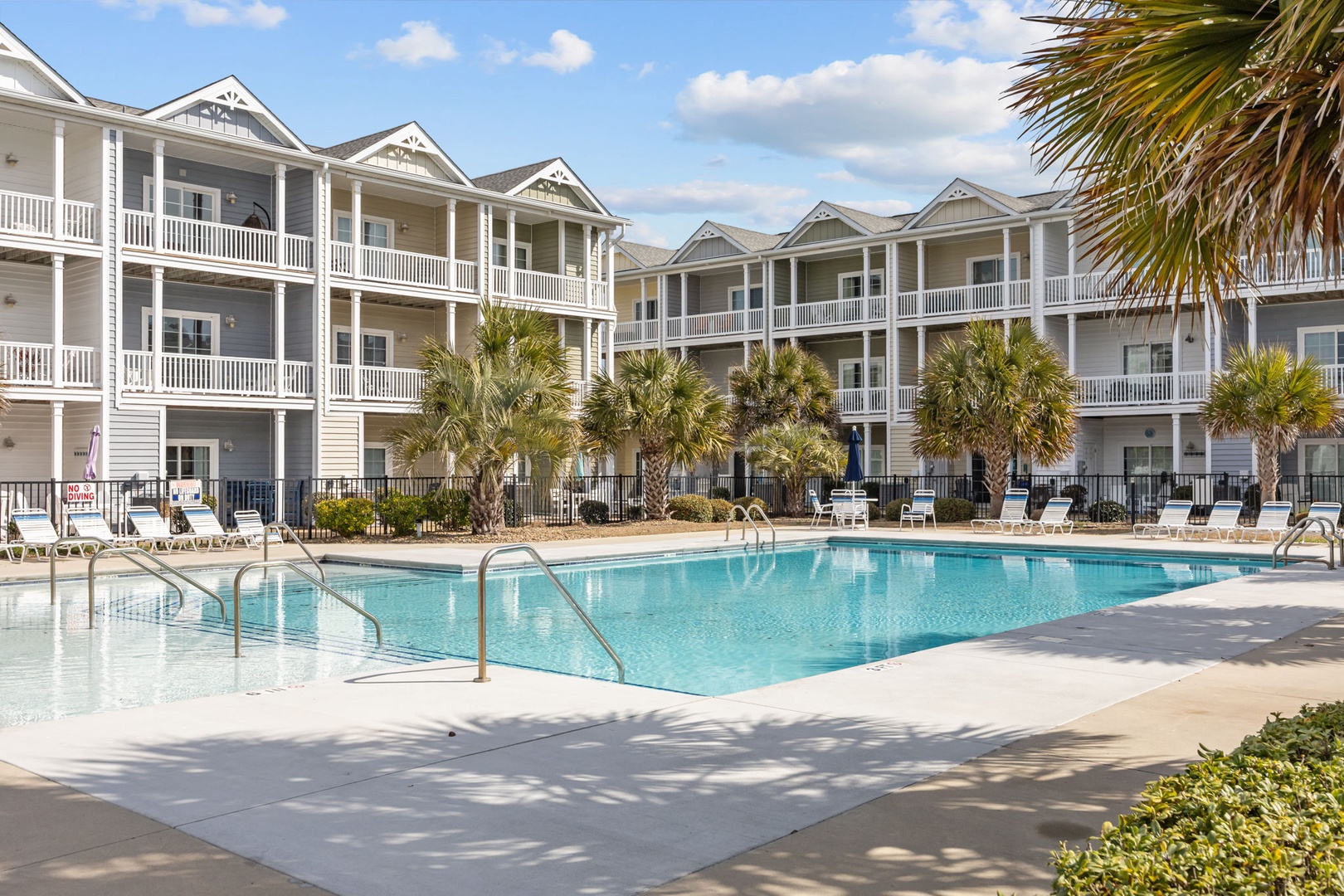 Multi-story coastal resort buildings surround a sparkling community pool, creating a classic beach town atmosphere.