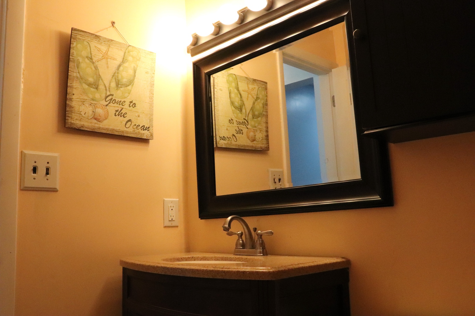 Your coastal-themed bathroom features a charming vanity with warm lighting and beach-inspired décor, creating a relaxing retreat after a day by the shore.