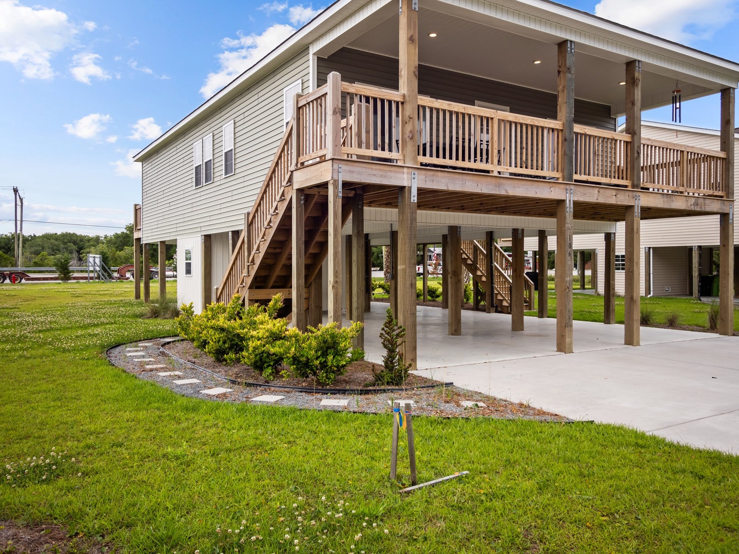 Coastal-style elevated home with spacious covered deck and convenient ground-level parking, surrounded by peaceful landscaped grounds.