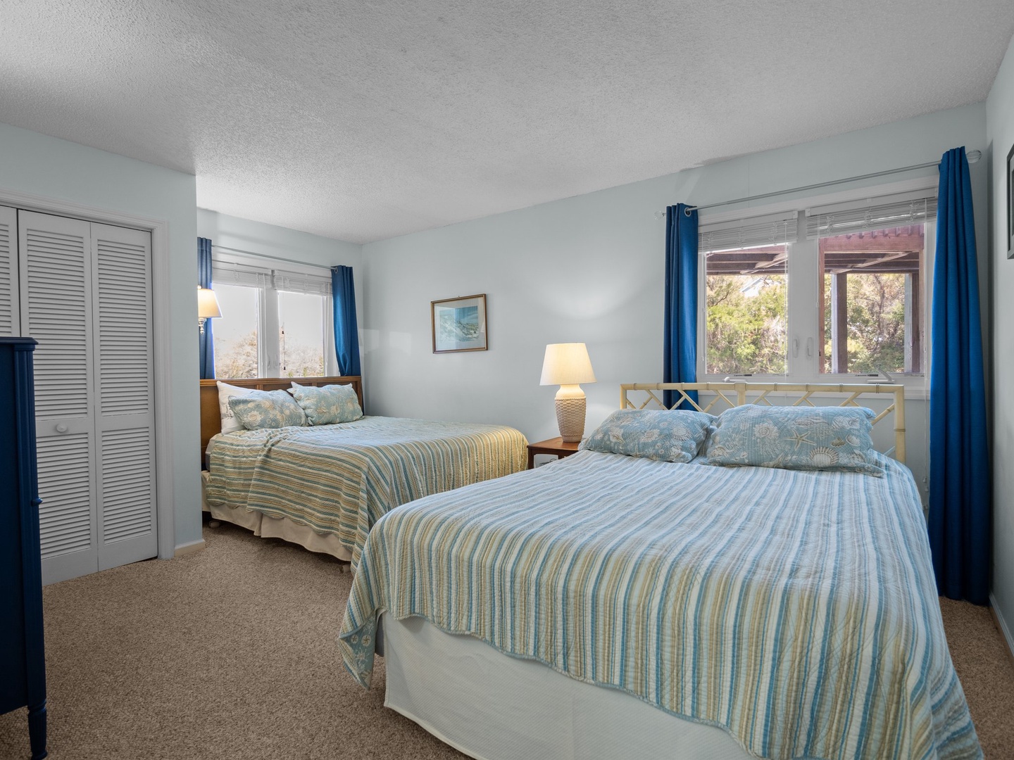 Wake up refreshed in your coastal-inspired bedroom featuring two comfortable beds with crisp striped linens and peaceful garden views.