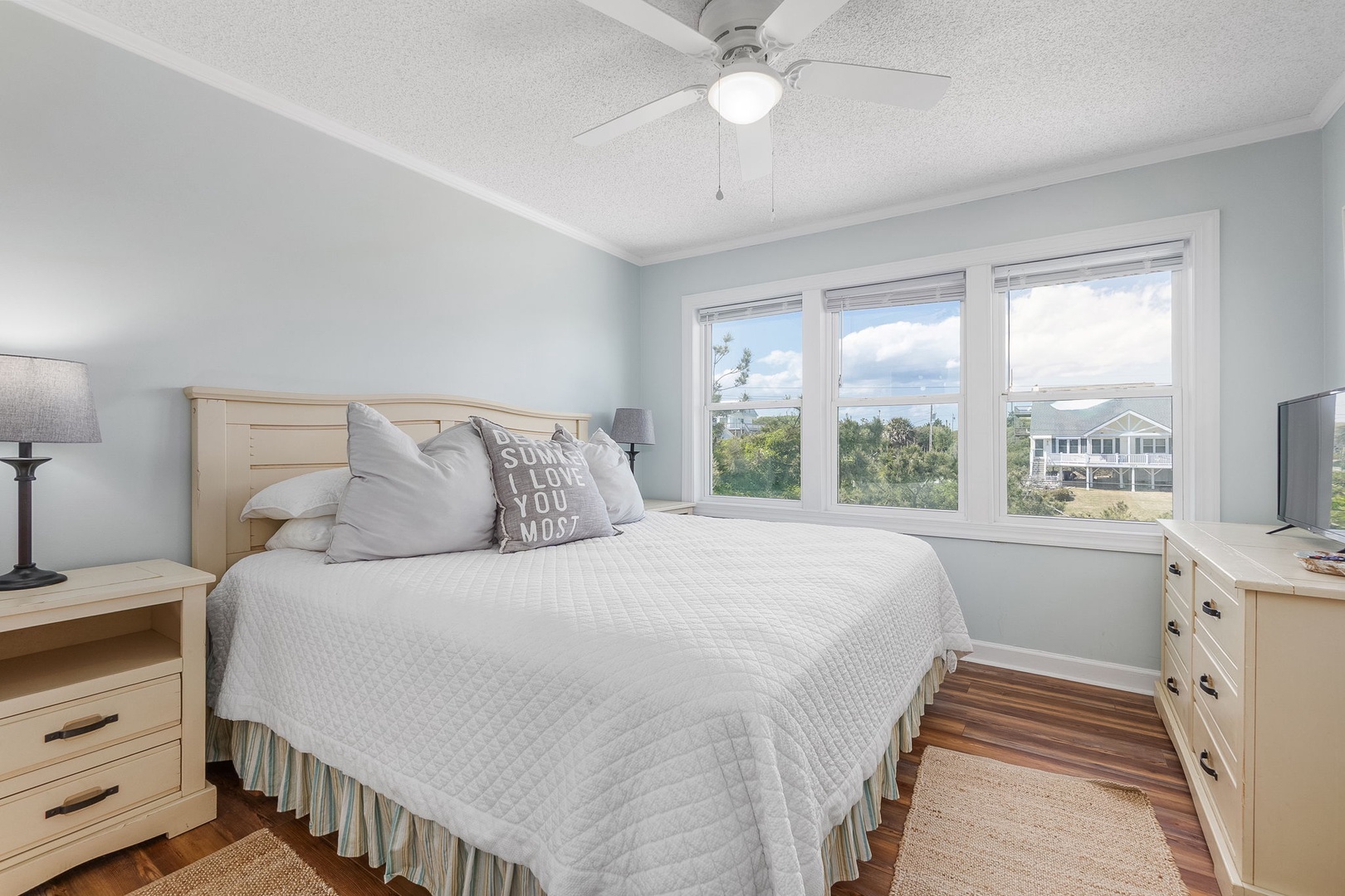 Wake up to serene views in your cozy bedroom, where natural light streams through large windows and a gentle ceiling fan keeps you comfortable.