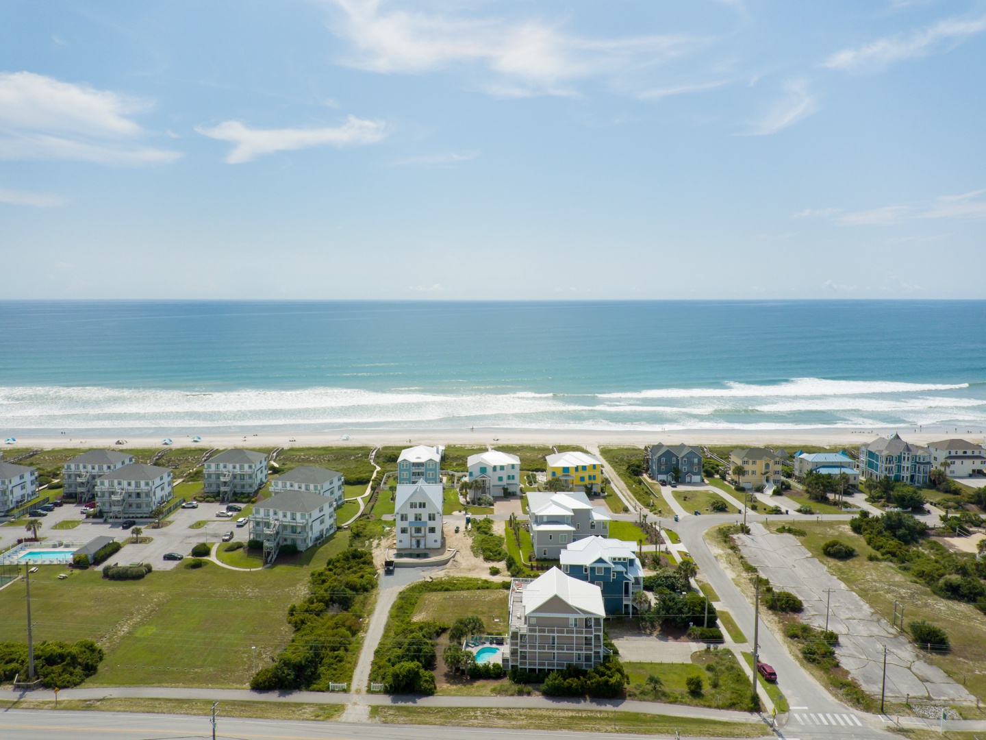 Aerial view of beachfront vacation homes nestled along pristine coastline with rolling waves and sandy shores stretching endlessly.