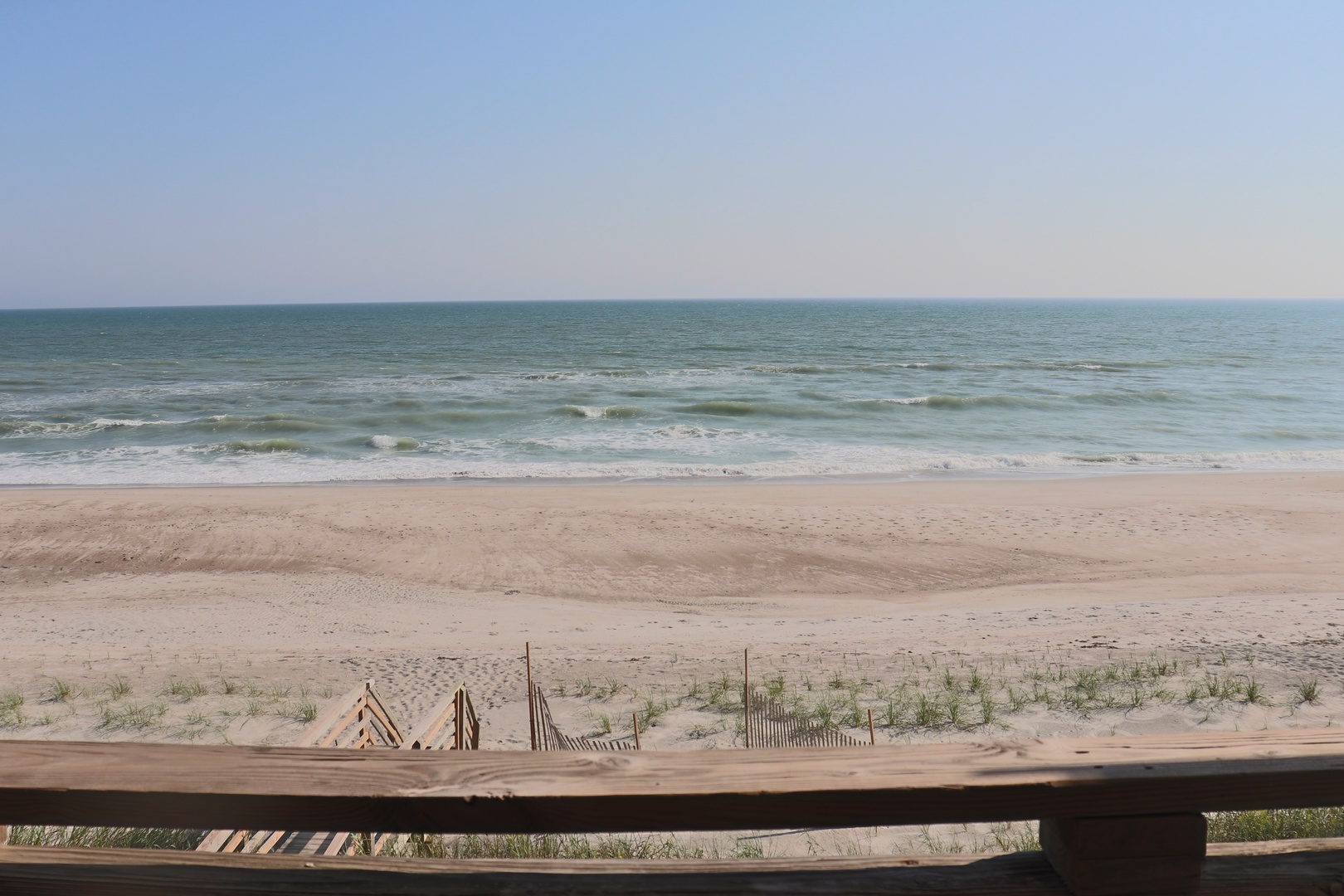 Pristine sandy beach stretches along the coastline with gentle waves and clear blue skies creating a peaceful coastal setting.