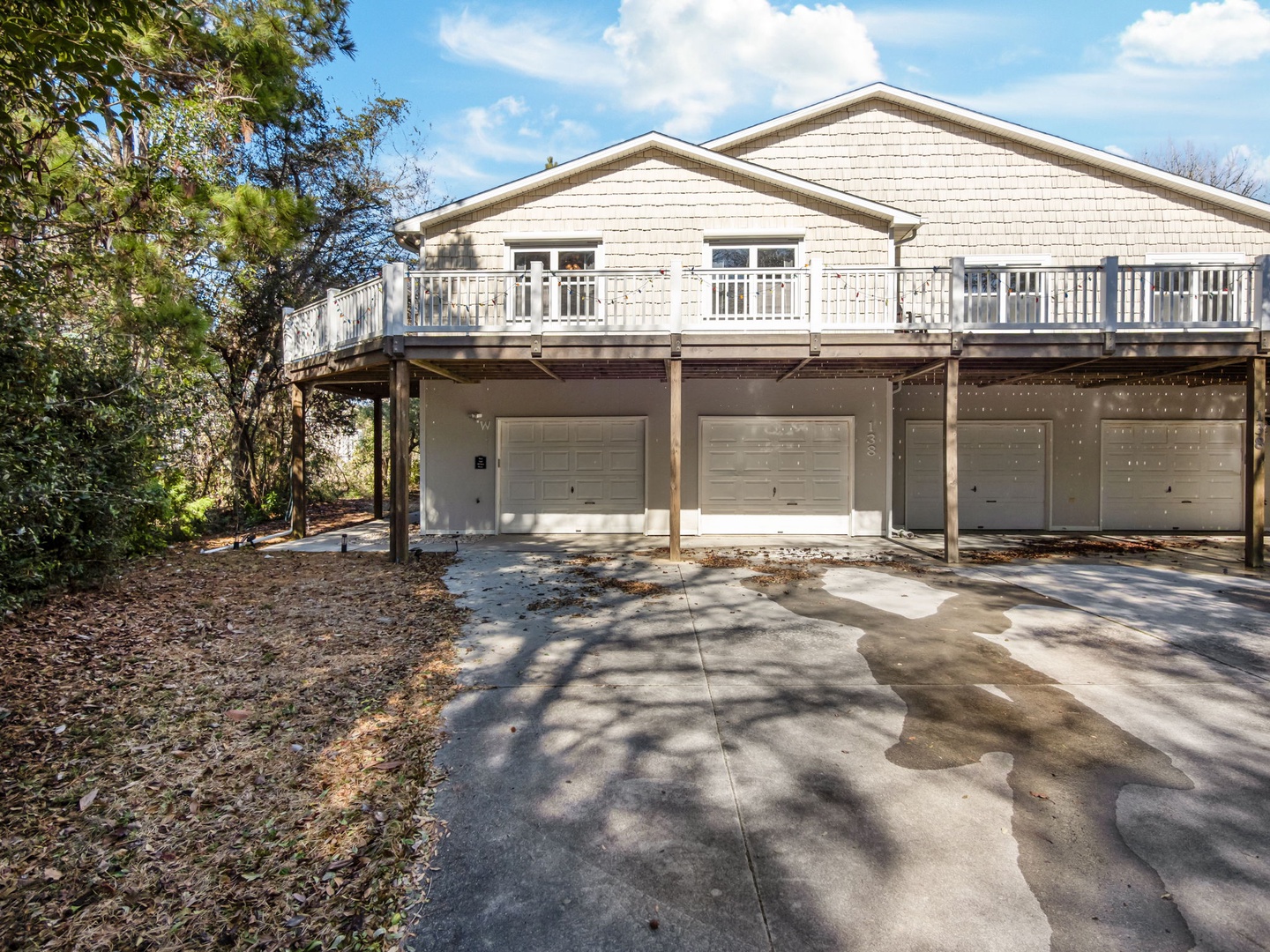 Spacious beachside property with multiple garage spaces and elevated deck balconies surrounded by mature trees and natural landscaping.