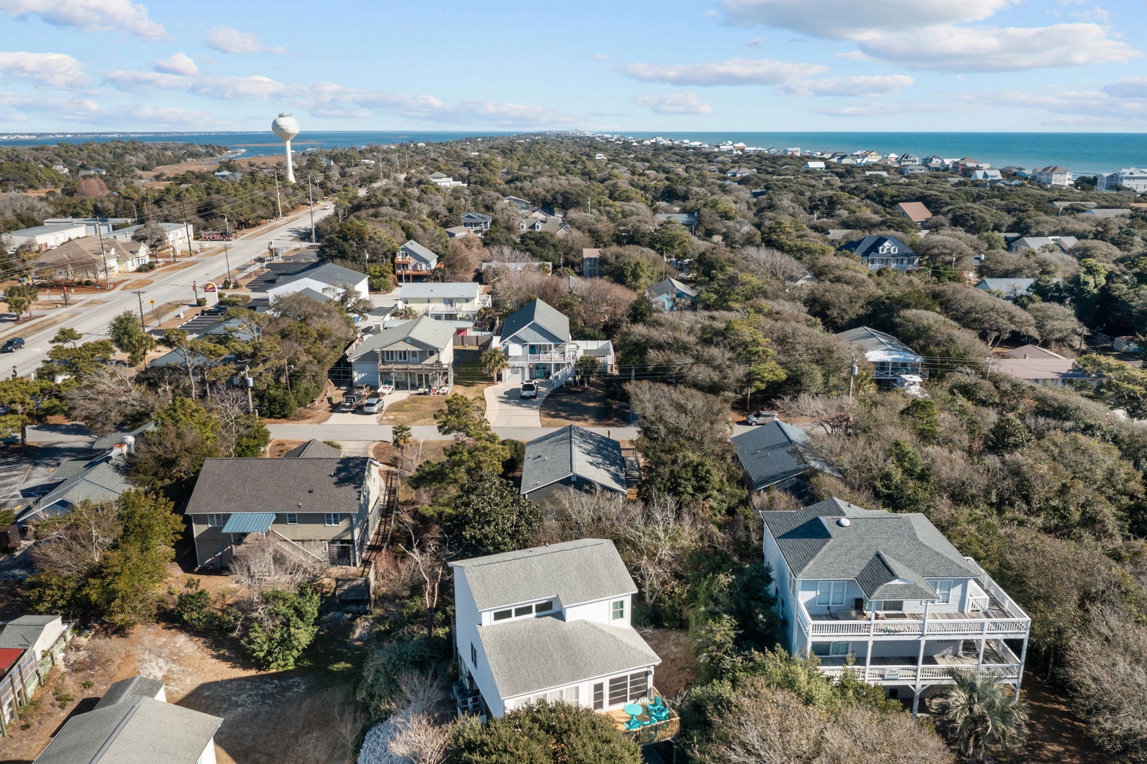 Coastal community with homes nestled among lush trees, featuring a distinctive water tower landmark and easy beach access.