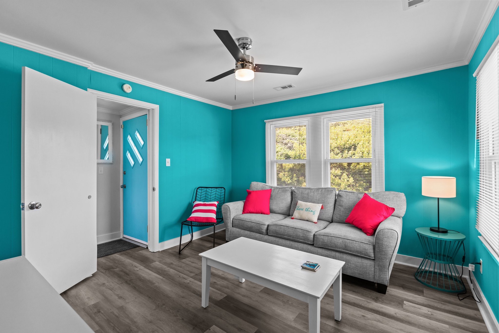 Unwind in your vibrant living space with bold turquoise walls and cozy gray sofa, where colorful pillows invite you to relax.