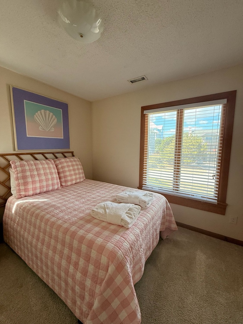 Step into your peaceful retreat with soft coastal touches and a crisp, welcoming bed dressed in fresh linens. Sunlight streams through the window, inviting you to unwind in comfort.