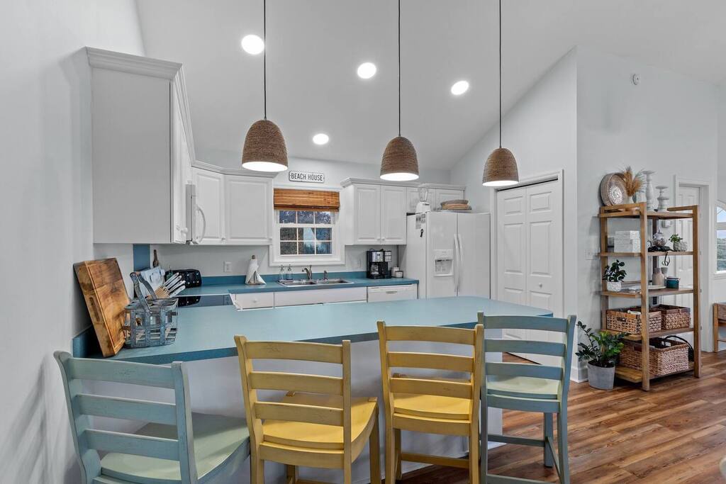 You'll love preparing meals in this bright, coastal-inspired kitchen with turquoise counters, modern appliances, and charming woven pendant lights.