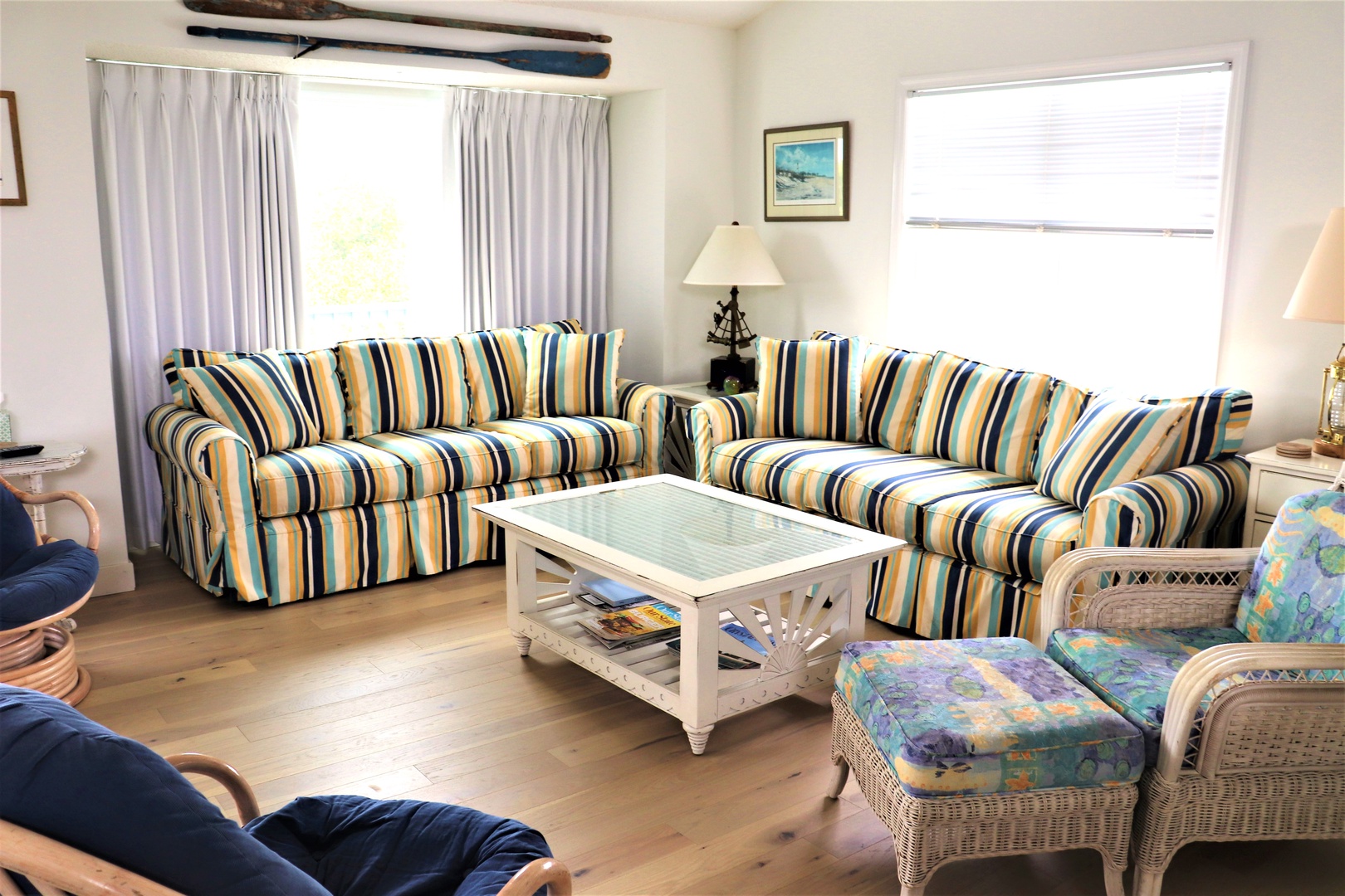 Relax in your bright living room featuring striped sofas, wicker chairs, and coastal artwork that perfectly captures your beachside getaway.