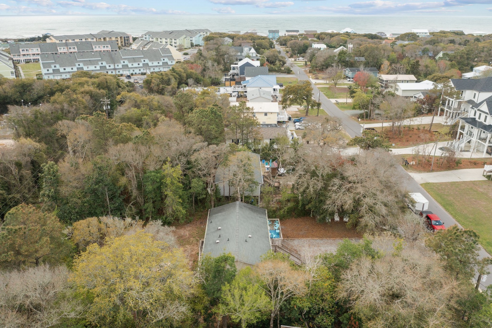 Aerial view showcasing the property's peaceful residential neighborhood setting among mature trees and nearby coastal community homes.
