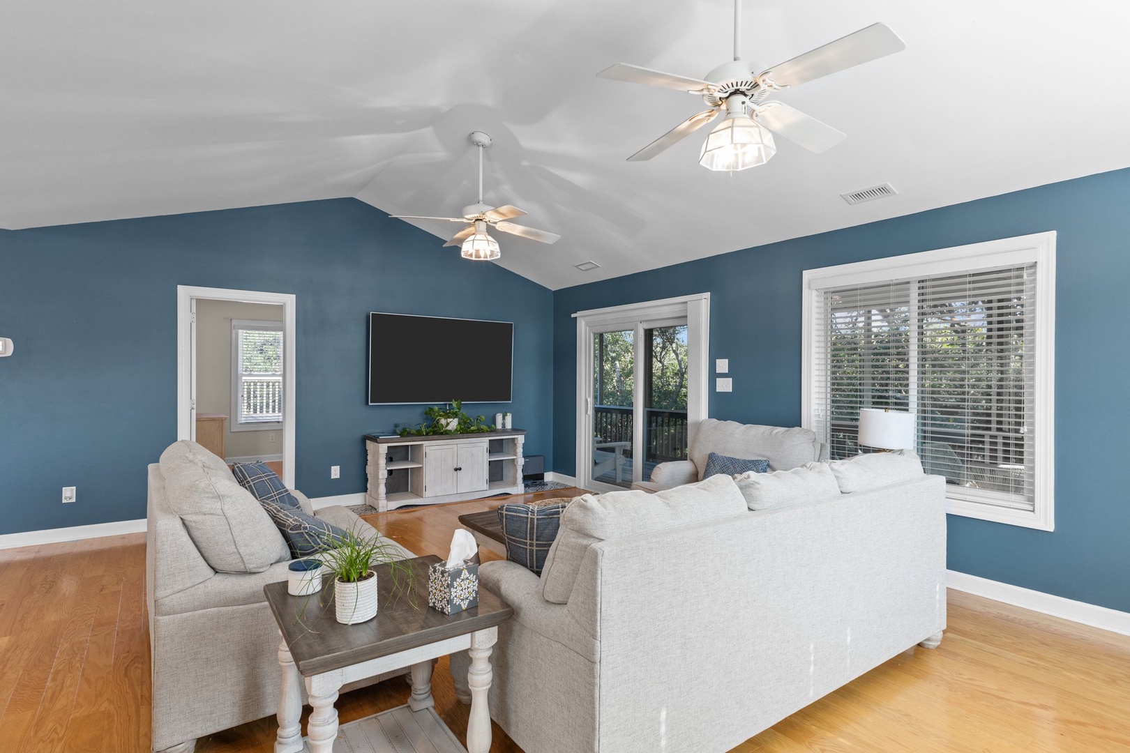 Relax in your spacious living room featuring cozy sectional seating, vaulted ceilings with ceiling fans, and peaceful views through large windows.