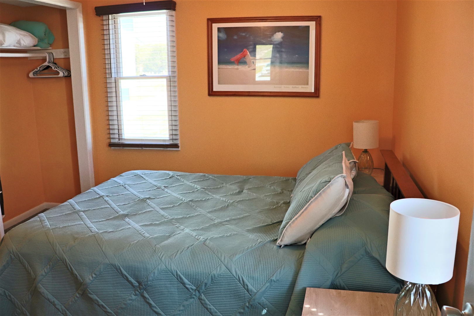 Your cozy bedroom features warm orange walls and comfortable bedding, with natural light streaming through your window and artwork to inspire peaceful mornings.