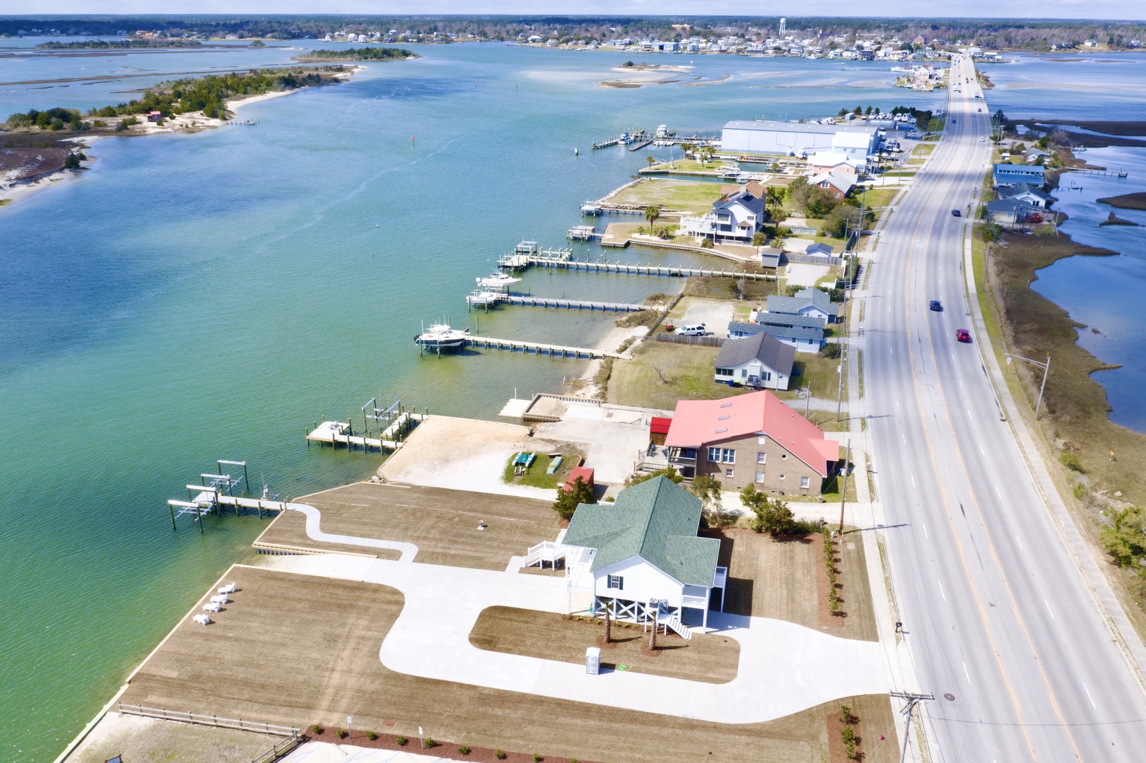 Aerial view of a charming waterfront community featuring pristine turquoise waters, private docks, and coastal homes along a scenic highway.