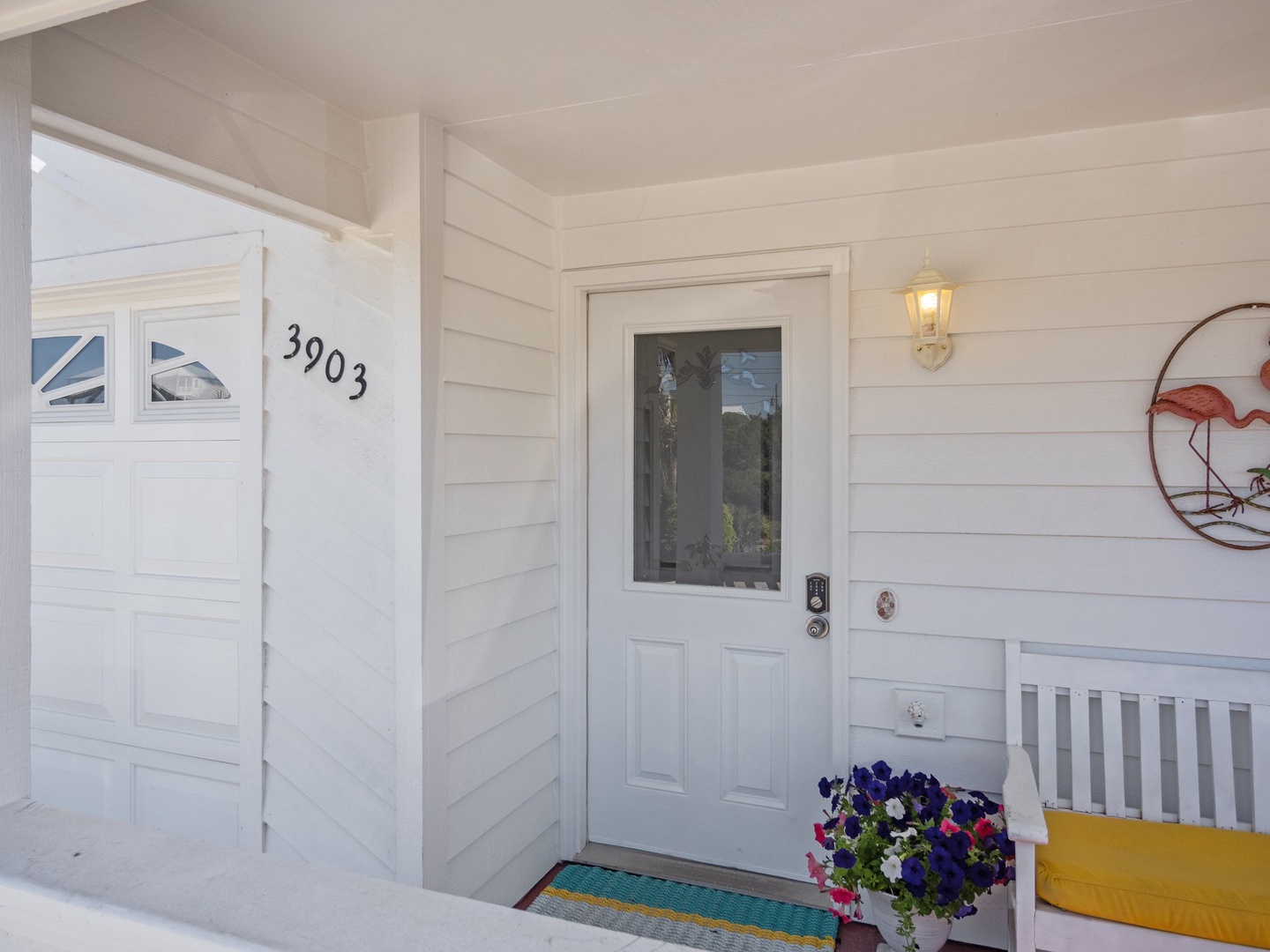 Charming white farmhouse entrance with welcoming front porch and colorful blooms to greet you upon arrival.