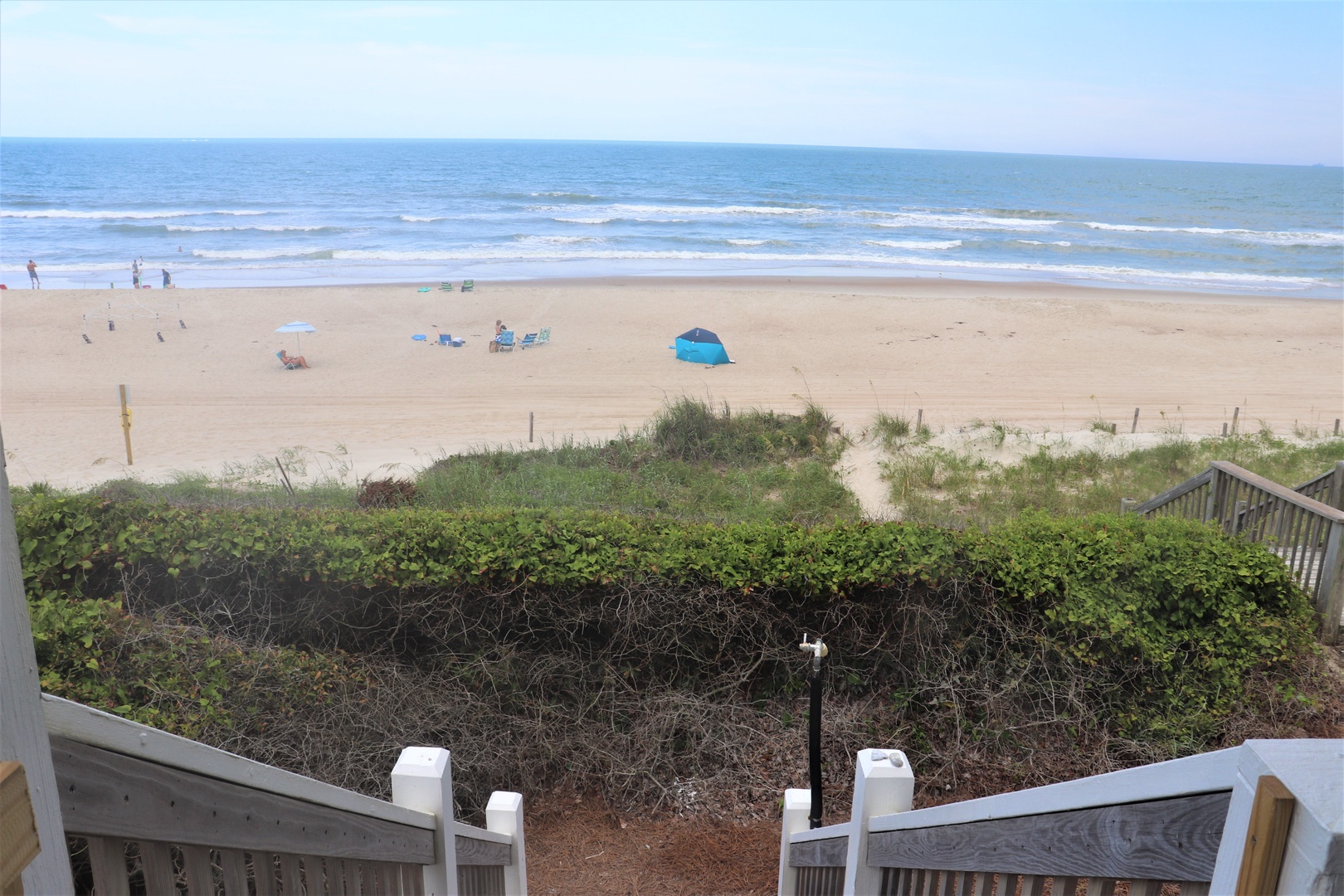 Expansive sandy beach stretches along the coastline with gentle waves and scattered beachgoers enjoying the pristine waterfront area.