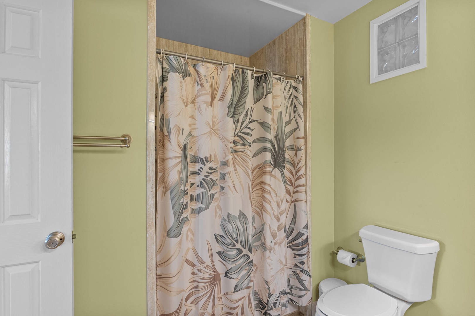 Step into your cheerful bathroom with tropical-print shower curtain and soothing green walls that create a refreshing oasis for your daily routine.