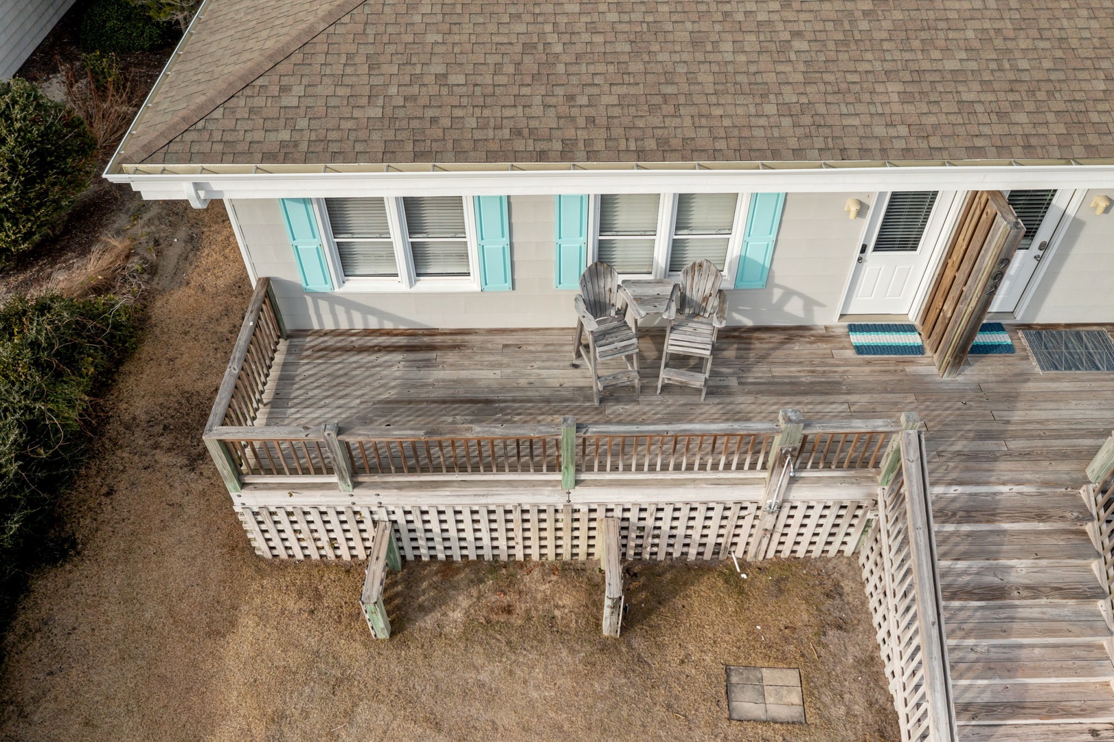 Aerial view of coastal rental property featuring spacious wooden deck with outdoor seating and turquoise shutters.