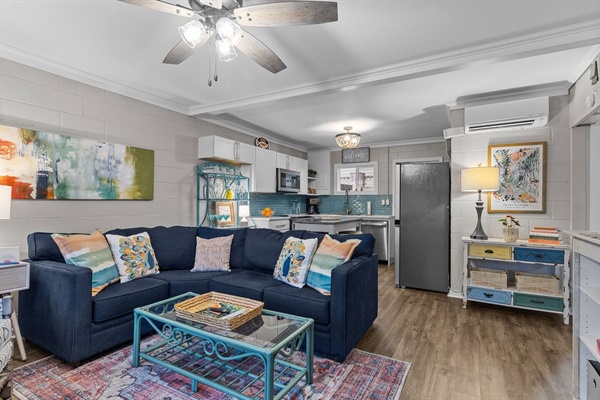 Relax in your thoughtfully designed living space where modern comfort meets style—plush navy sofa, open kitchen, and charming ceiling fan create your perfect home base.